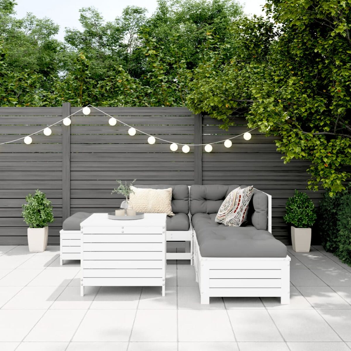 Weißes Outdoor-Sofaset mit grauen Kissen und Kissen. Ein weißer Couchtisch und Pflanzen auf einer Terrasse.