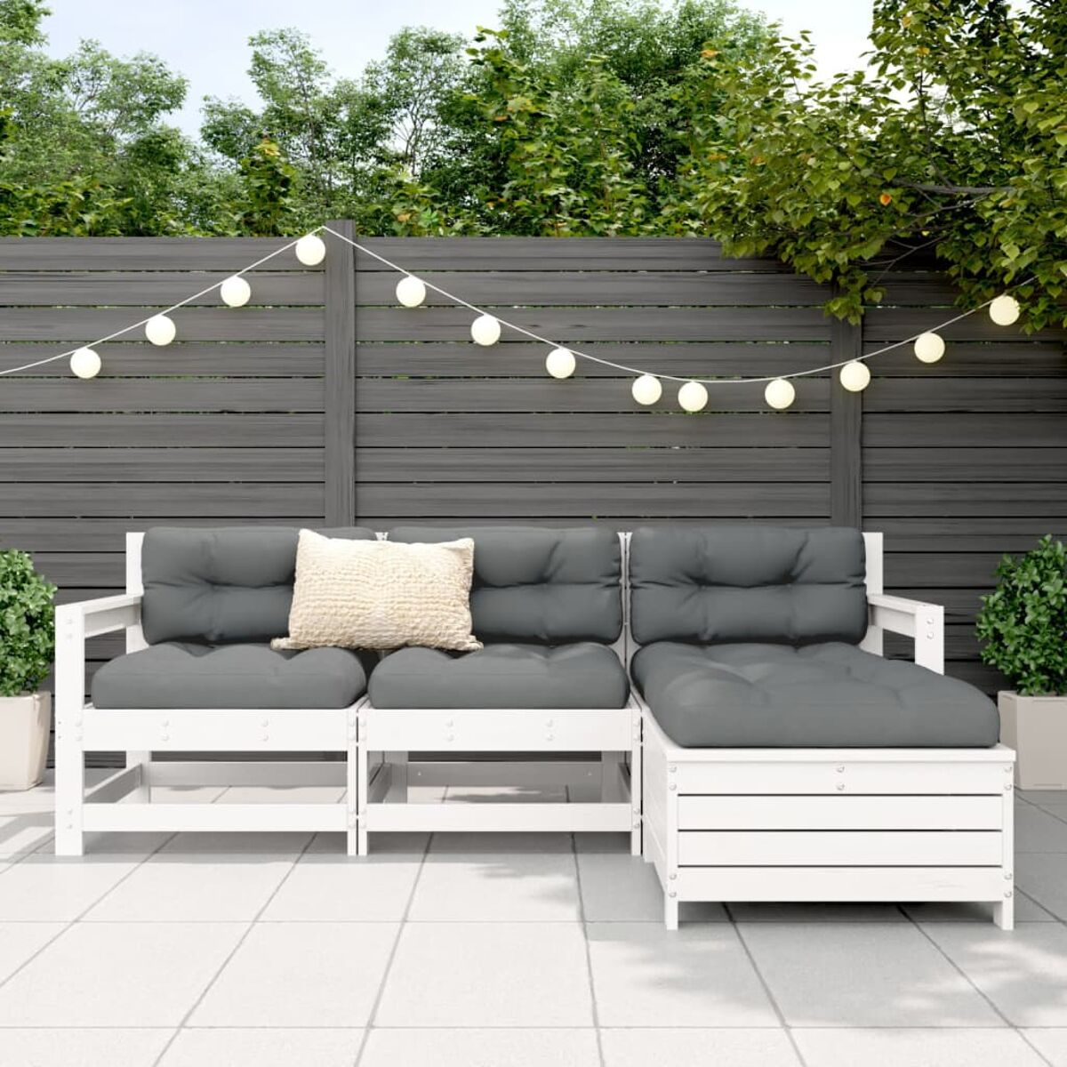 Ecksofa für den Außenbereich, weißer Rahmen, graue Kissen, Lichterkette und Grün im Hintergrund.