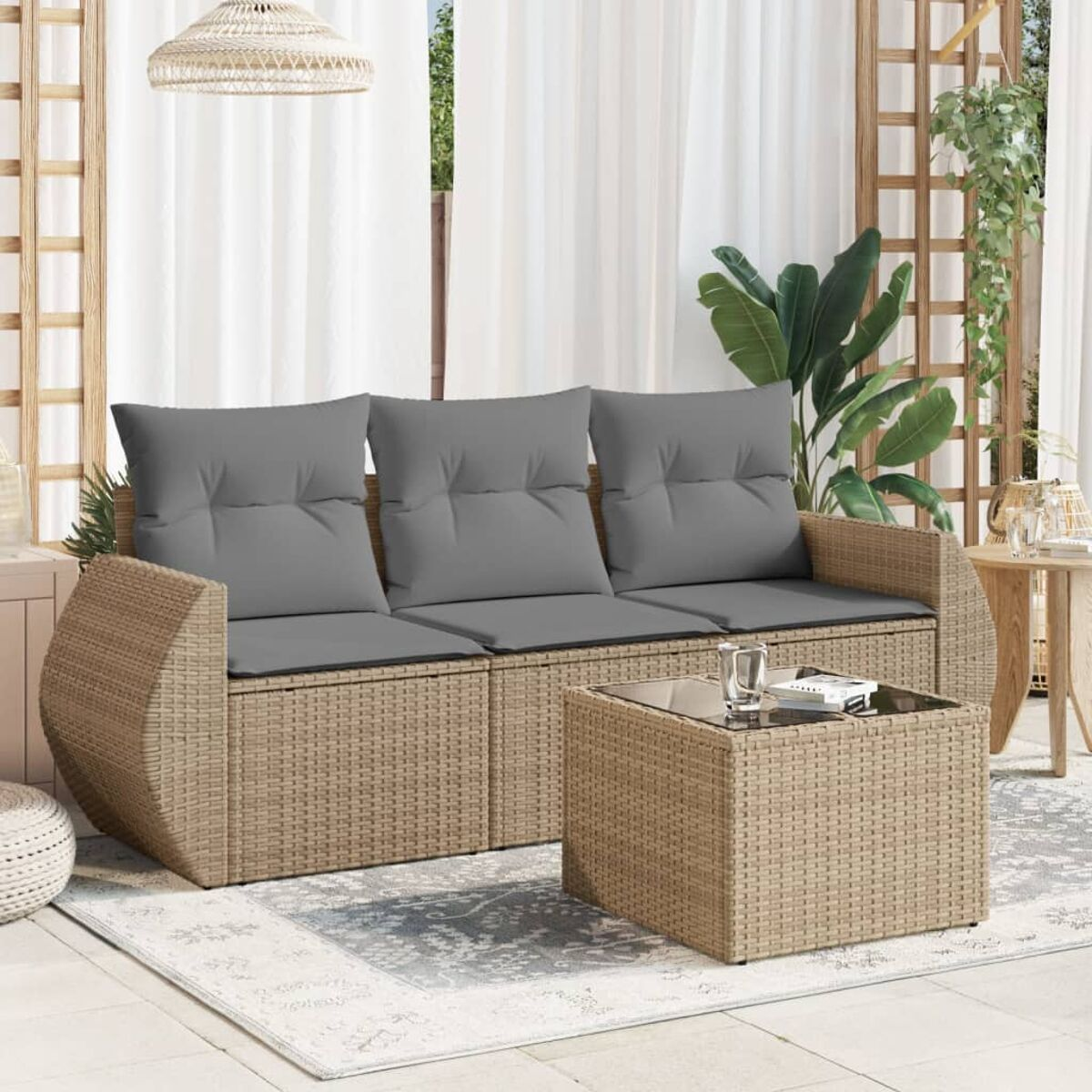 Rattanmöbel im Freien. Graue Kissen auf einem Ecksofa und einem Glastisch. Hintergrund hat Vorhänge und Pflanzen.
