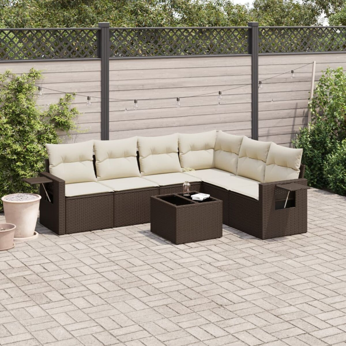 Braunes Outdoor-Ecksofa aus Korbgeflecht mit beigen Kissen. Auf einer Backstein-Terrasse mit Grün.