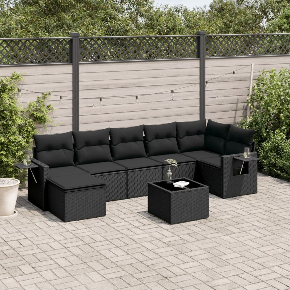 Schwarzes Outdoor-Ecksofa aus Korbgeflecht mit Couchtisch und Beistelltischen auf einer Ziegelterrasse.