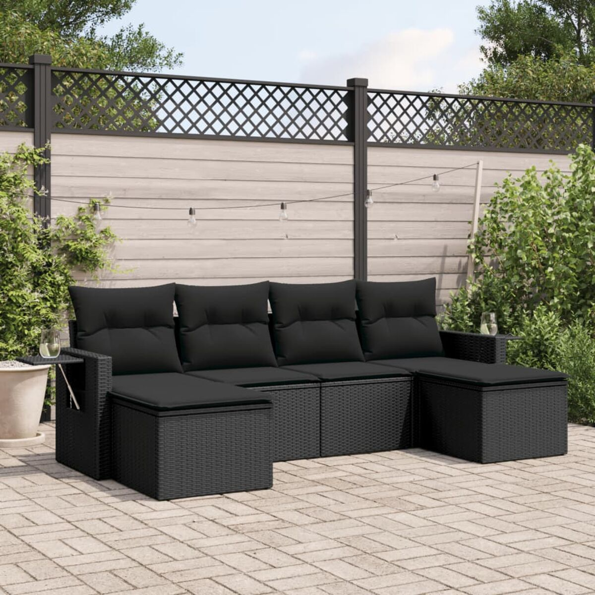 Schwarzes Korbgeflecht-Ecksofa-Set mit schwarzen Kissen, auf einer Backstein-Terrasse, mit Lichterketten.