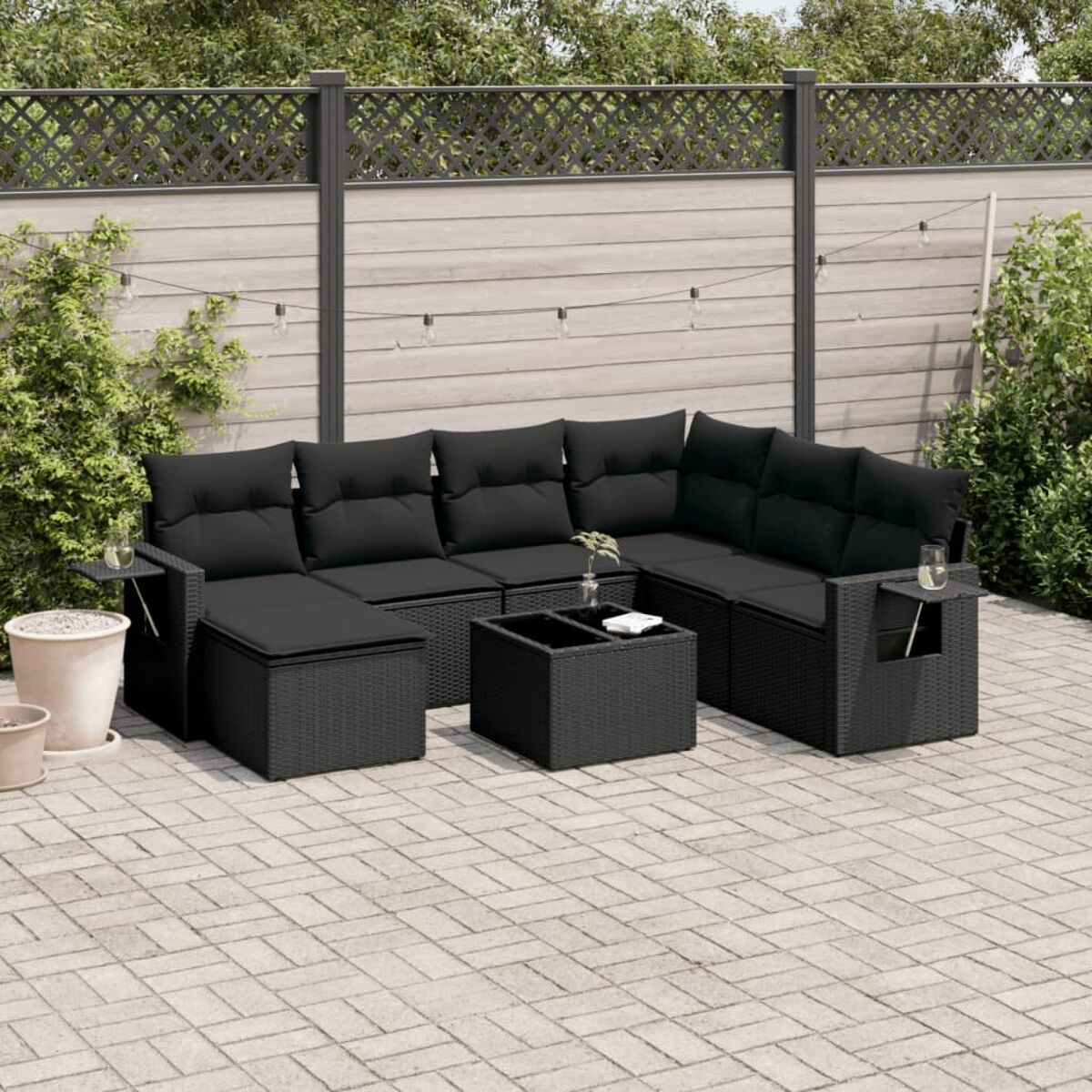 Schwarzes Rattan-Ecksofa mit schwarzen Kissen, einem Tisch und einer Backstein-Terrasse im Garten.