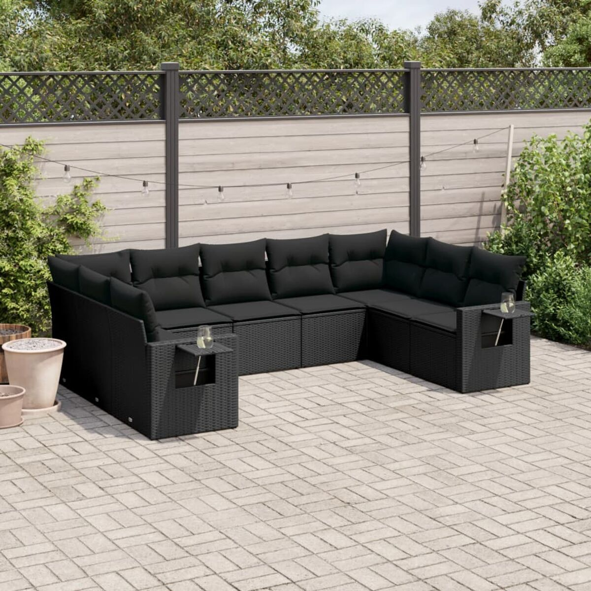 Schwarzes Outdoor-Sofa aus Korbgeflecht auf der Terrasse. Inklusive Beistelltisch. Umzäunter Hintergrund mit Pflanzen.
