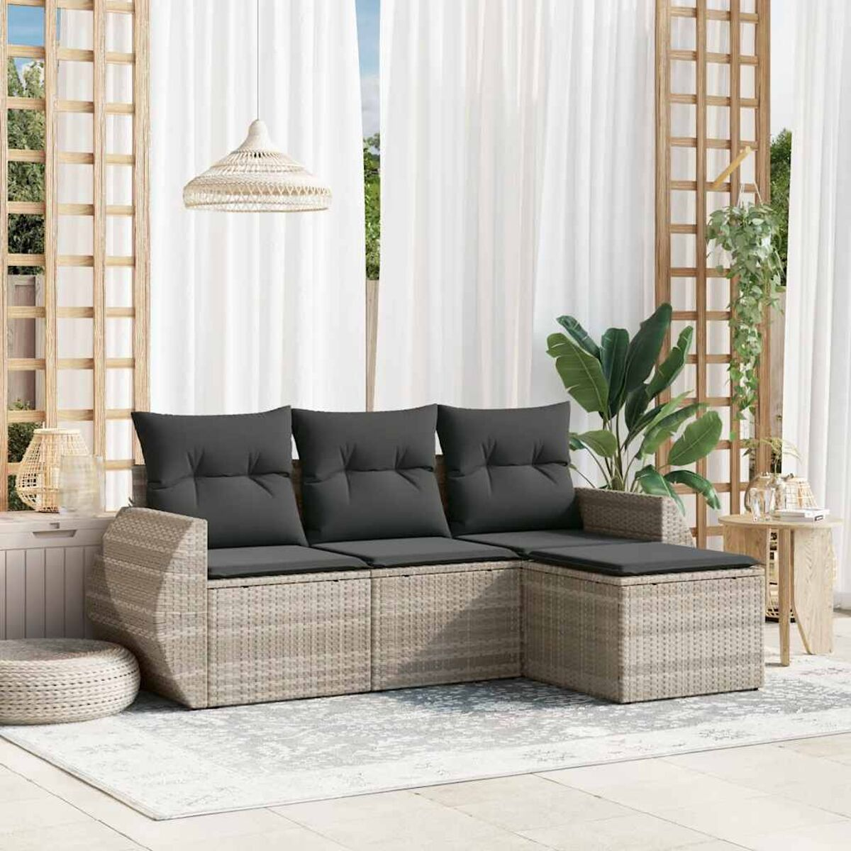 Geflochtenes Ecksofa mit grauen Kissen auf einer Terrasse. Weiße Vorhänge im Hintergrund.