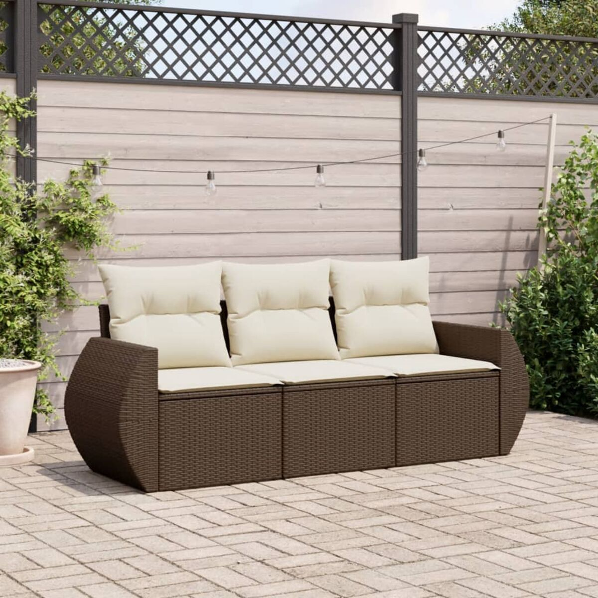 Divano in vimini marrone con cuscini color crema. Su un patio in mattoni, ambiente esterno.