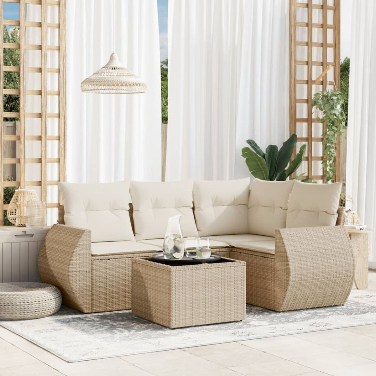 Beiges Ecksofa aus Korbgeflecht mit cremefarbenen Kissen und einem quadratischen Tisch. Es befindet sich auf einer Terrasse mit weißen Vorhängen.