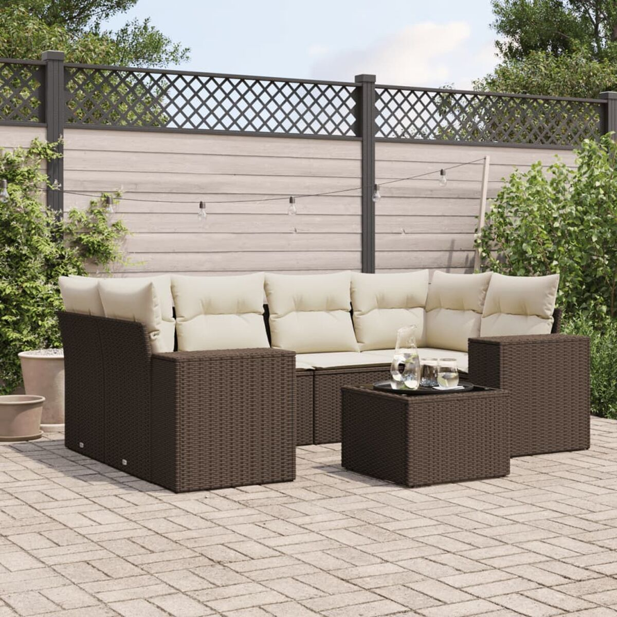 Terrassenset mit braunem Korbgeflecht, beigen Kissen und einem Couchtisch. Ziegel-Terrasse mit grünen Pflanzen.