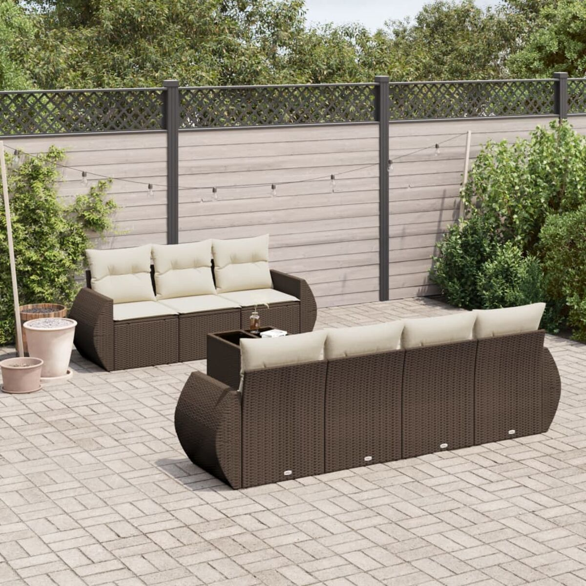 Braunes Outdoor-Sofaset mit weißen Kissen. Backstein-Terrasse. Grüne Pflanzen.