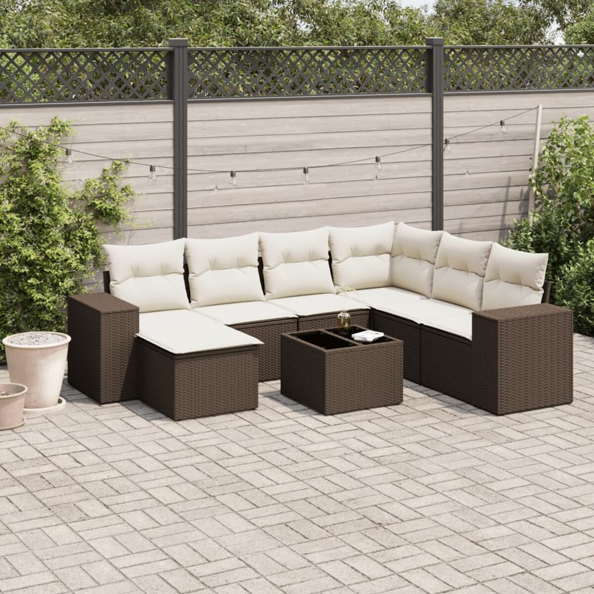 Set divano per esterni, vimini marrone scuro, con cuscini color crema. Un tavolino al centro, su un patio.