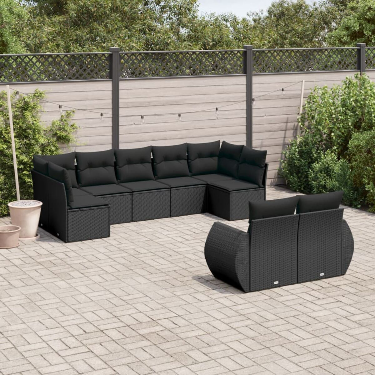 Schwarzes Outdoor-Ecksofa-Set aus Korbgeflecht auf einer Ziegelterrasse mit dunklem Zaun und Pflanzen.