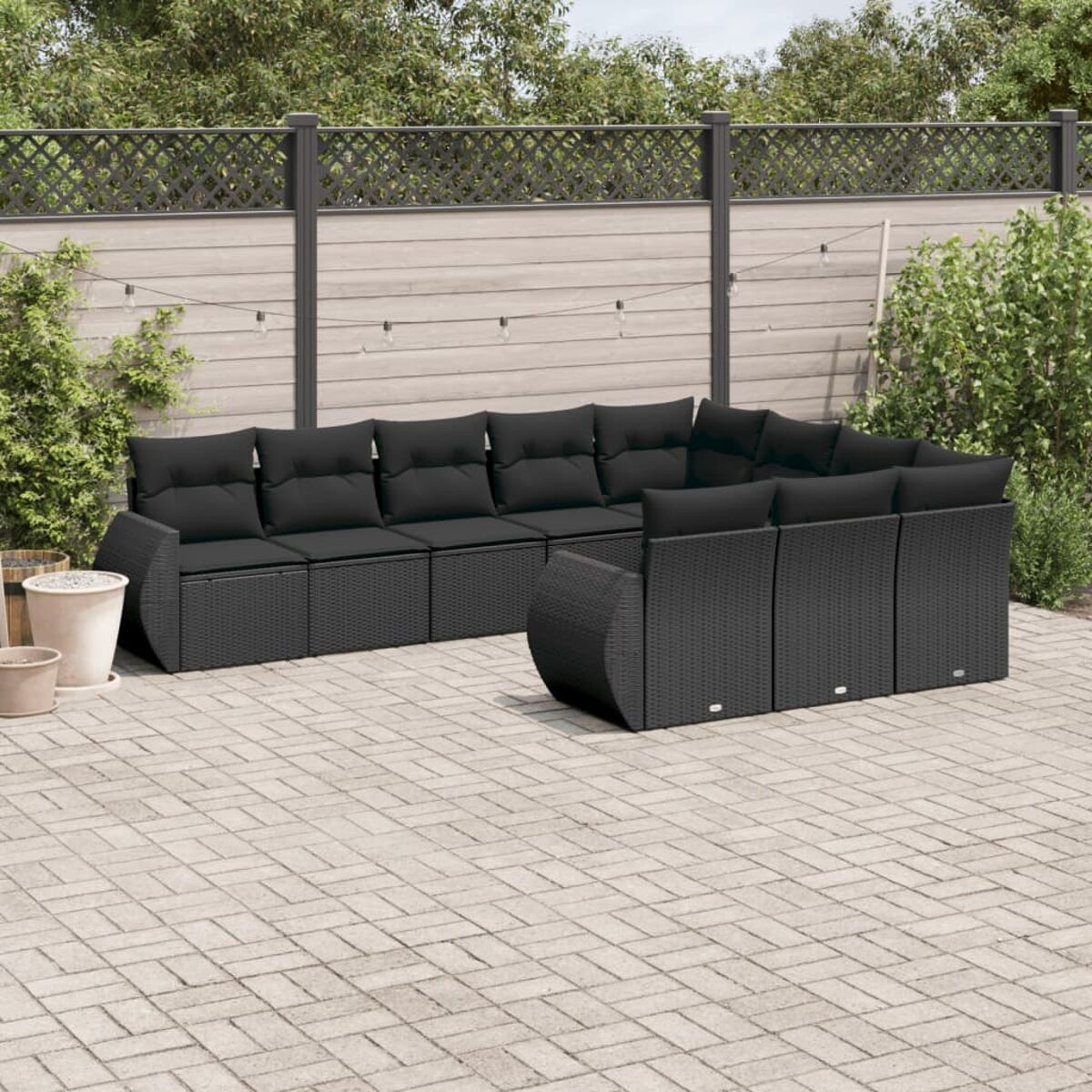 Schwarzes Rattan-Outdoor-Sofaset auf einer gepflasterten Terrasse mit Zaun und Pflanzen.