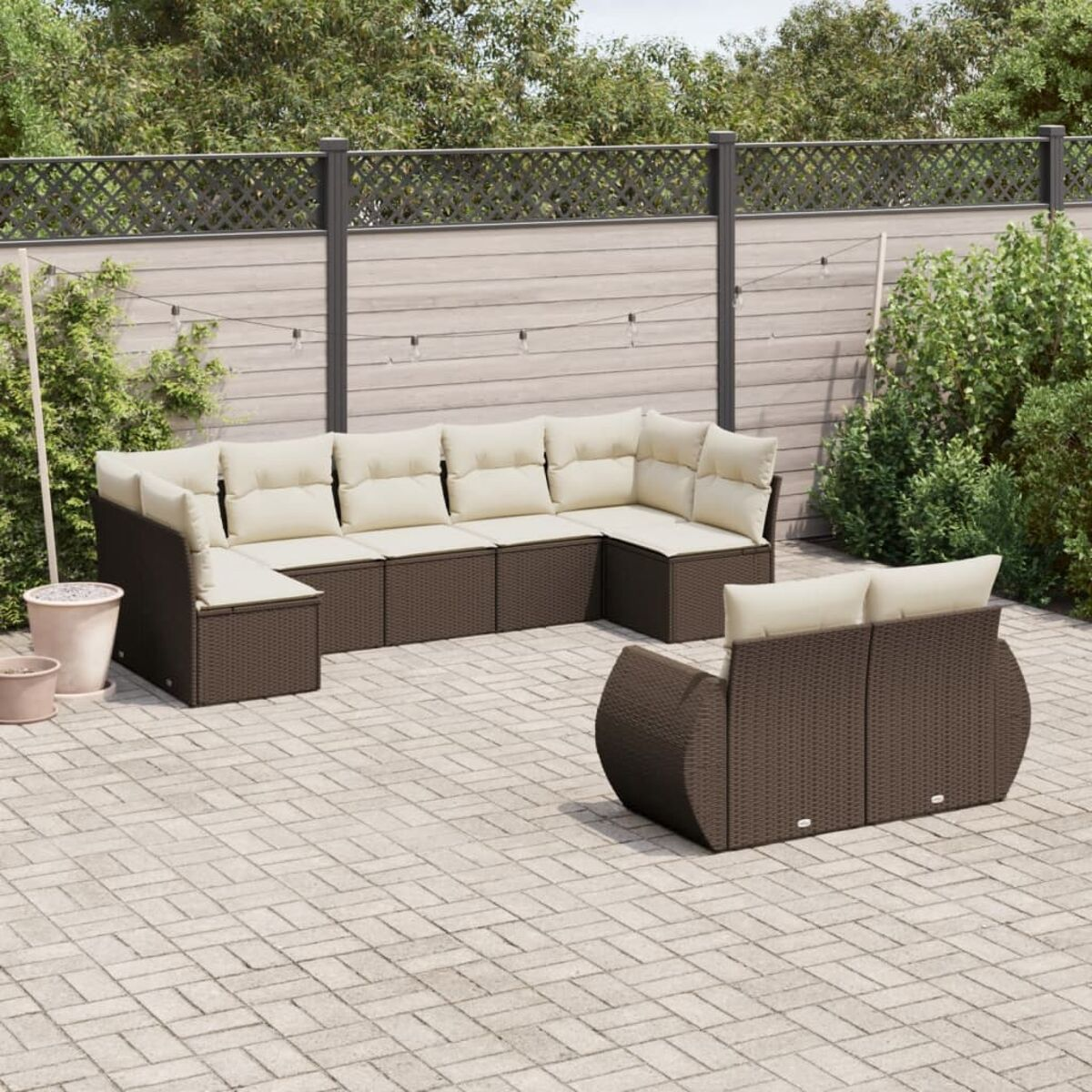 Set divano angolare in vimini marrone con cuscini crema su patio in mattoni. Sfondo verde.