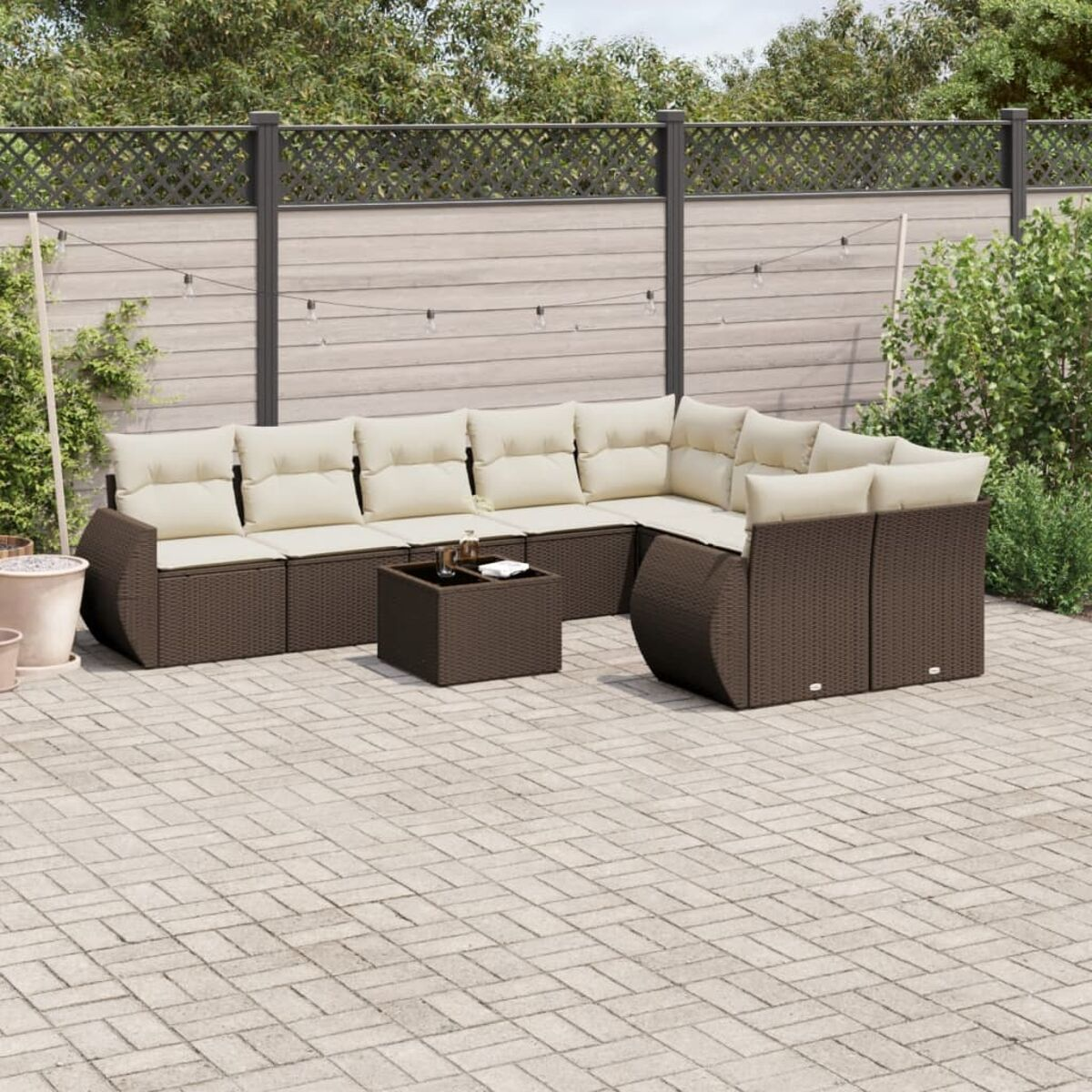 Set di sedute da esterno in rattan marrone con cuscini beige su un patio pavimentato con recinzione.