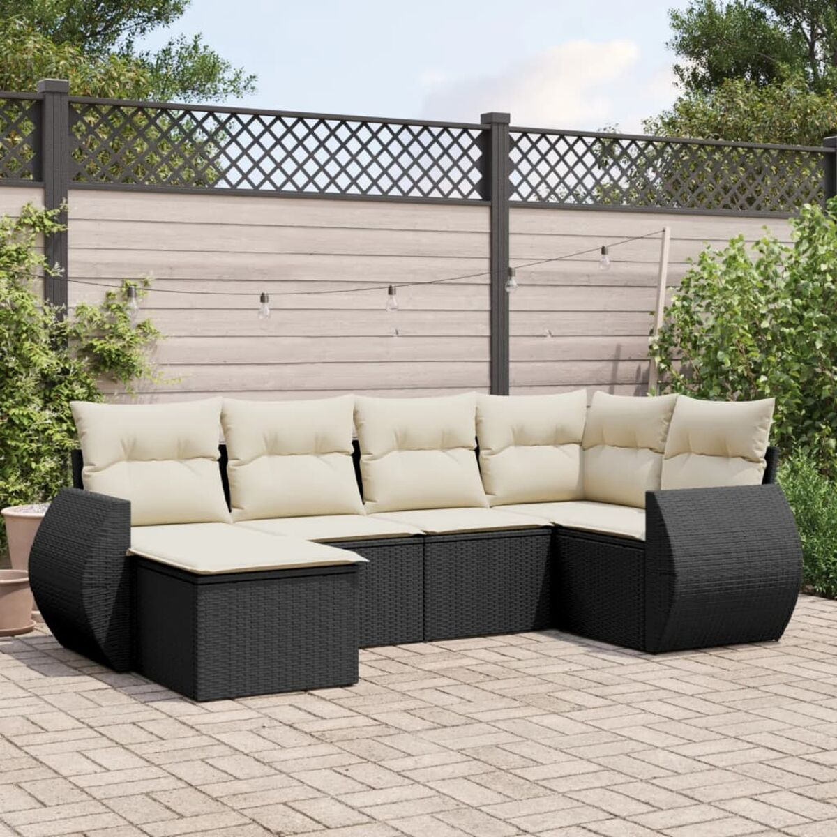 Schwarzes Rattan-Outdoor-Sofa mit cremefarbenen Kissen. Die Terrasse hat Ziegelboden und Zaun.