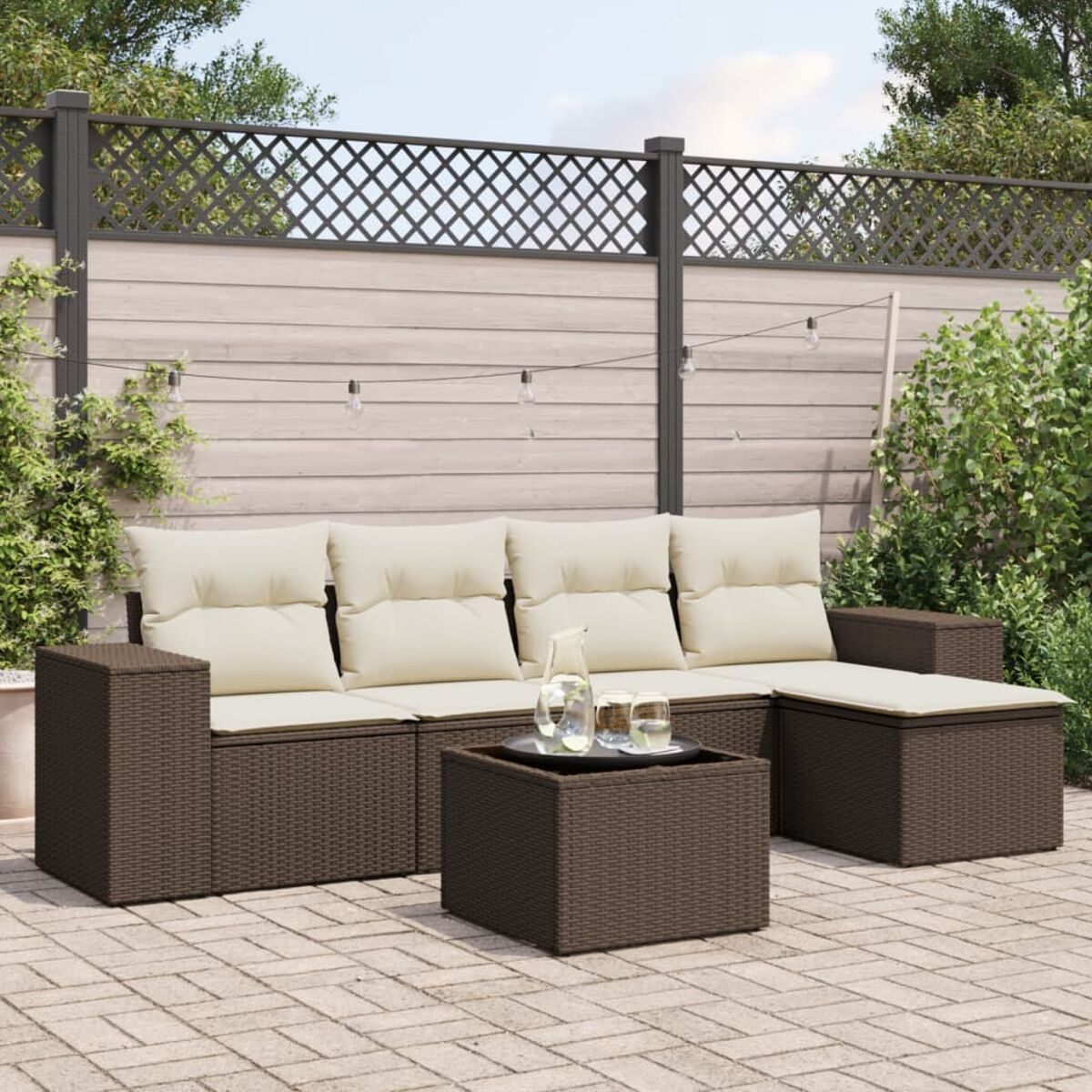 Divano componibile in rattan marrone scuro con cuscini color crema e tavolo su un patio in mattoni. Ambiente esterno.