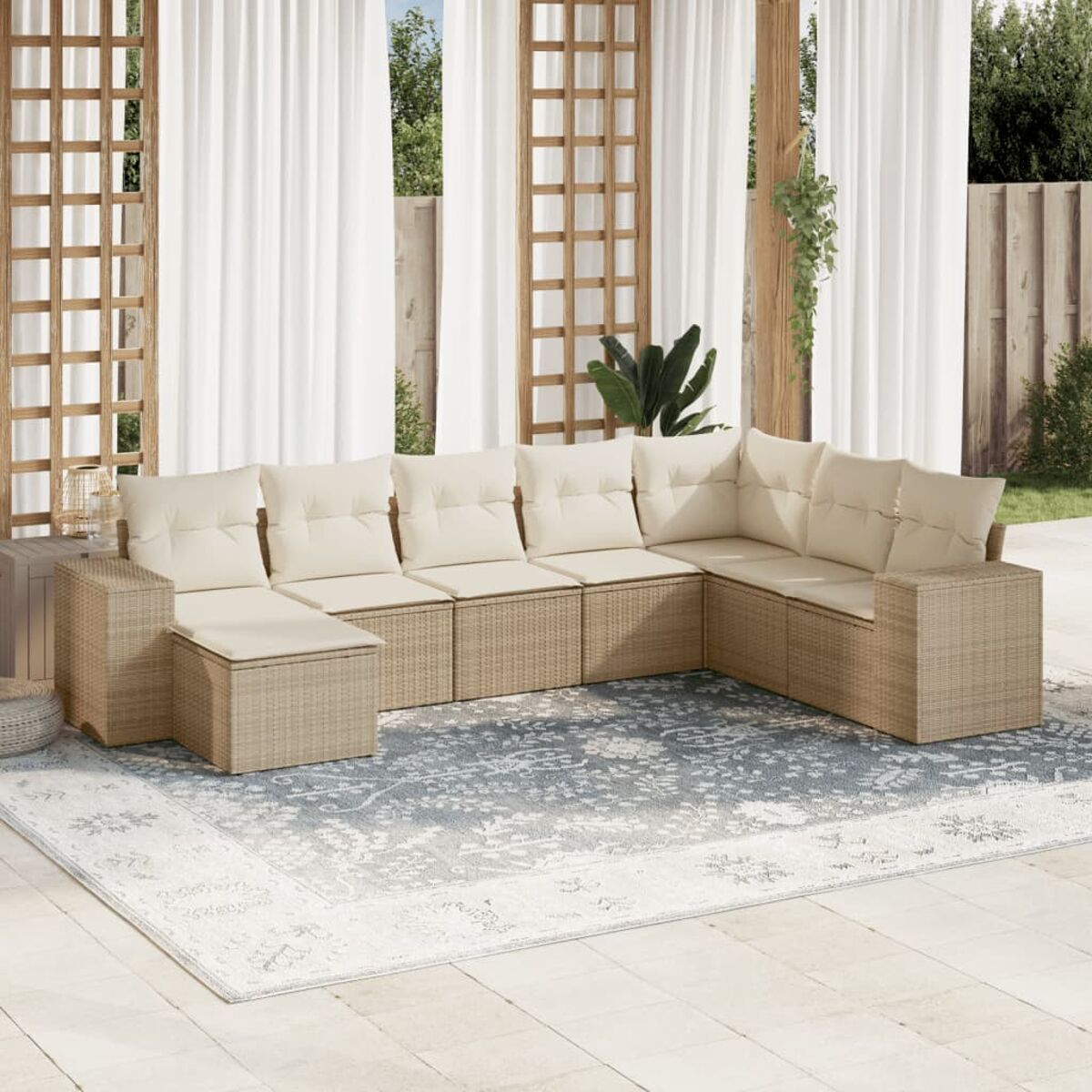 Geflecht-Terrassensofa mit cremefarbenen Kissen auf einer Terrasse mit Teppich und Vorhängen im Hintergrund.