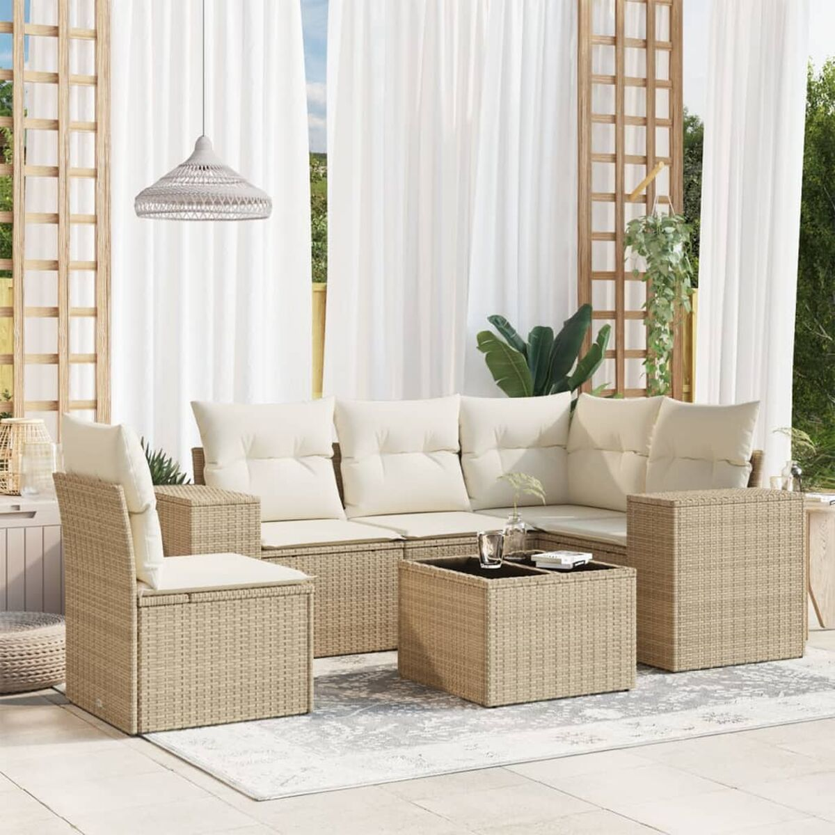Rattanset im Freien mit beigen Kissen und einem quadratischen Tisch. Weiße Vorhänge und Pflanzen im Hintergrund.