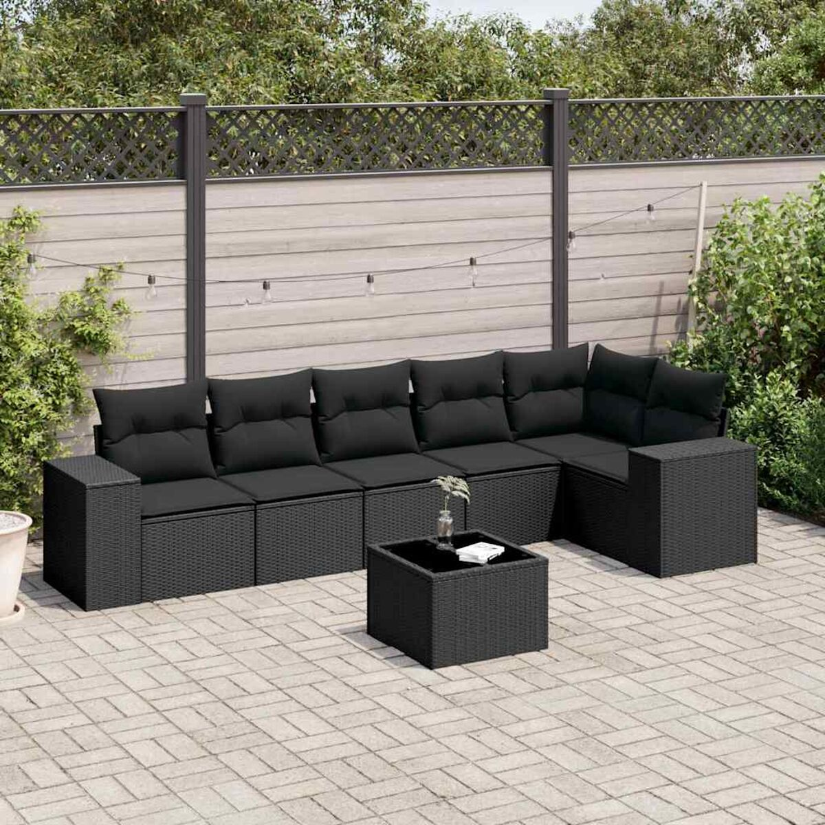 Schwarzes Rattan-Sofa-Set im Freien mit Kissen und einem Couchtisch. Das Set steht auf einer Backstein-Terrasse.