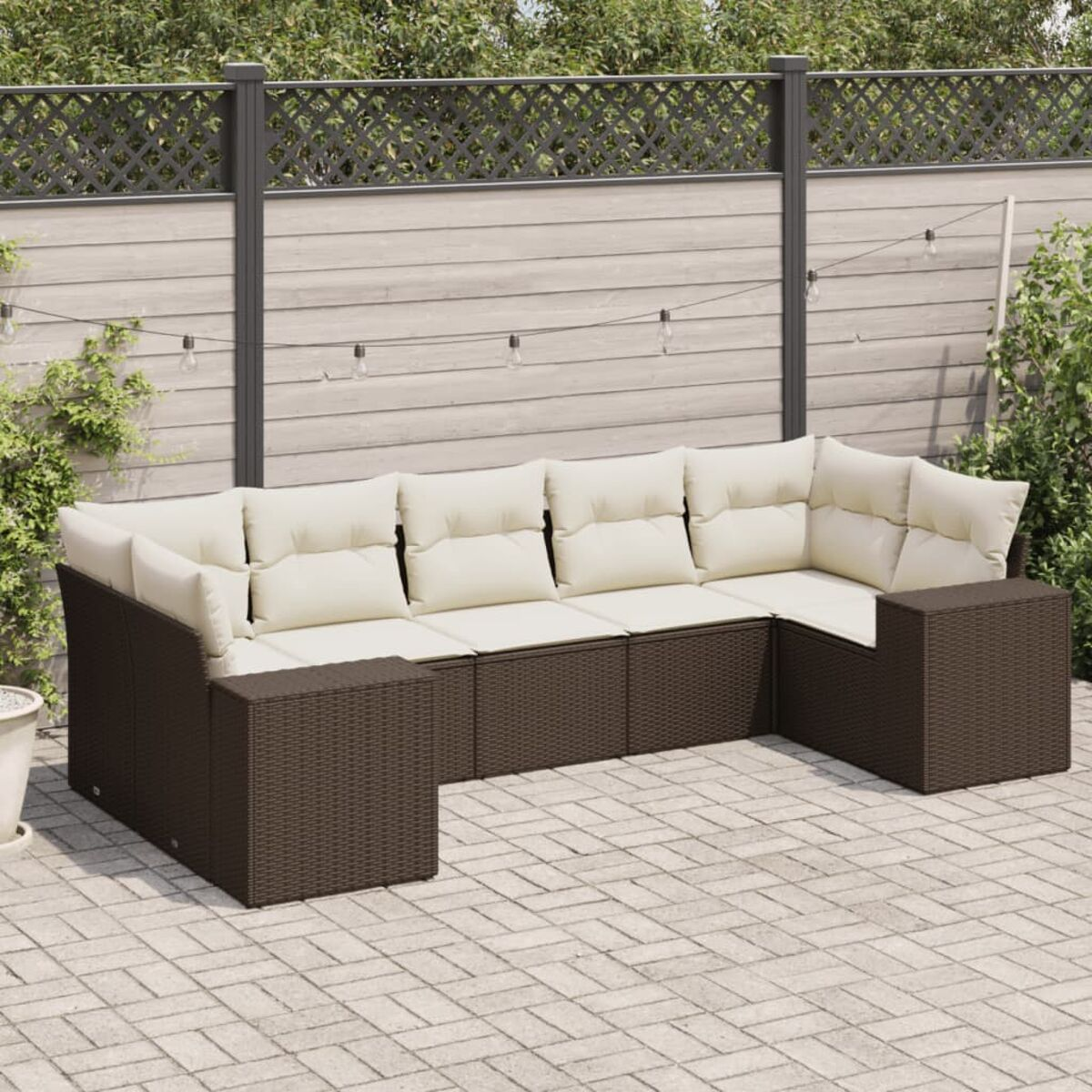 Divano angolare in rattan marrone scuro con cuscini color crema. Verde e recinzione sullo sfondo.
