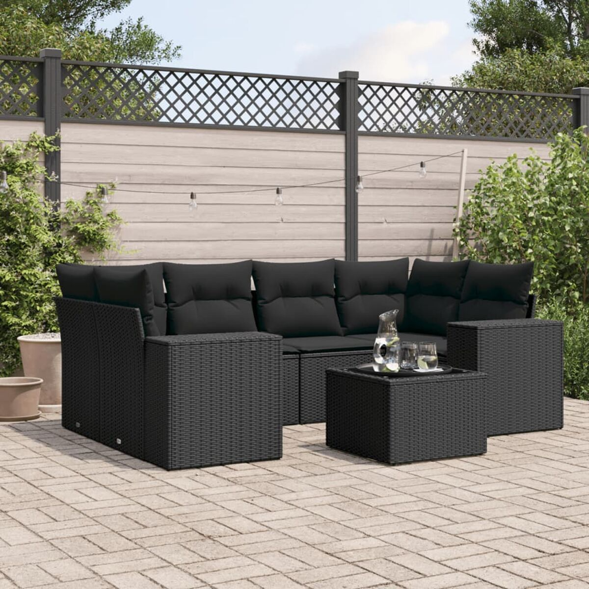 Schwarzes Ecksofa aus Korbgeflecht für den Außenbereich mit schwarzen Kissen und einem Couchtisch, auf einer Ziegelterrasse.