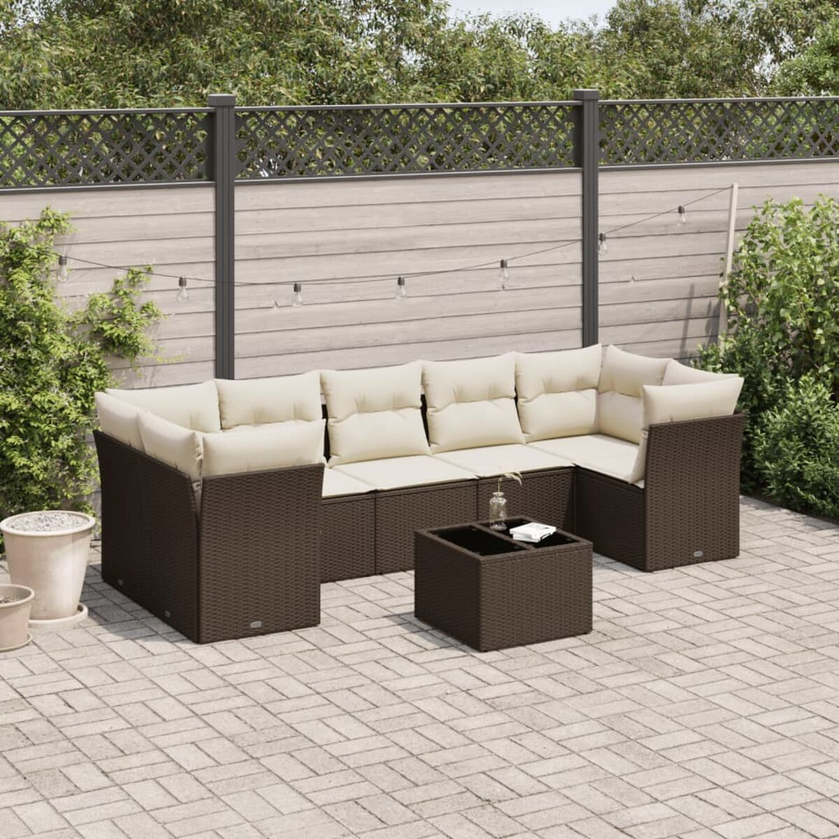 Terrassen-Set im Freien. Braunes Korbgeflecht mit beigen Kissen. Enthält Sofa, Stühle und Tisch. Holzzaun.