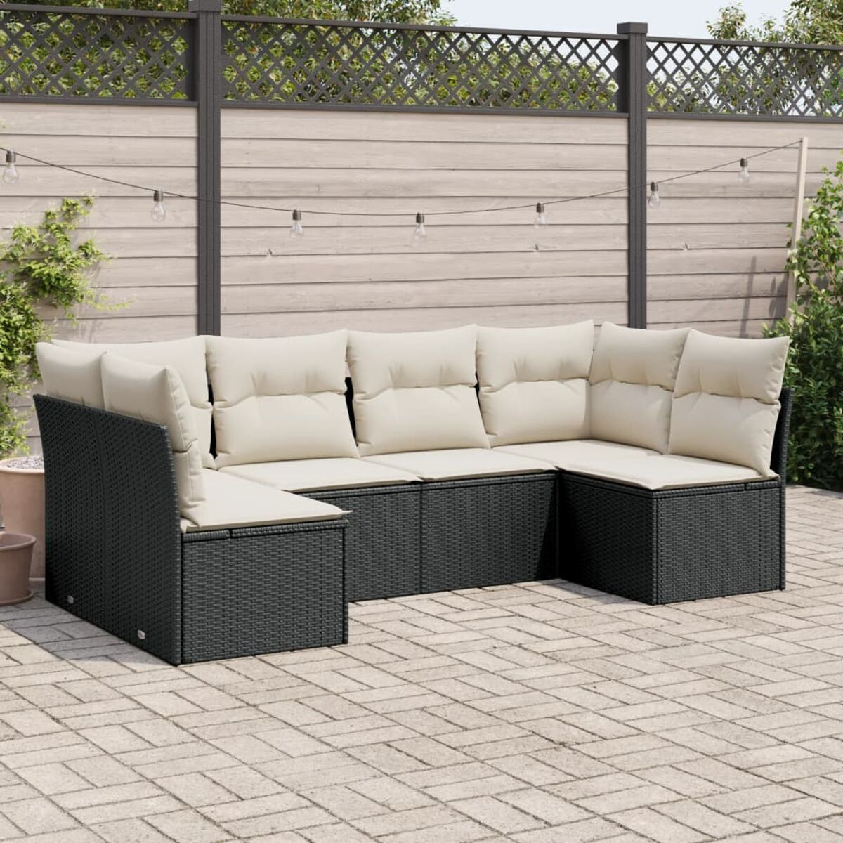 U-förmiges dunkles Rattan-Sofaset mit cremefarbenen Kissen auf einer Ziegelterrasse, Zaun und Lichterketten.