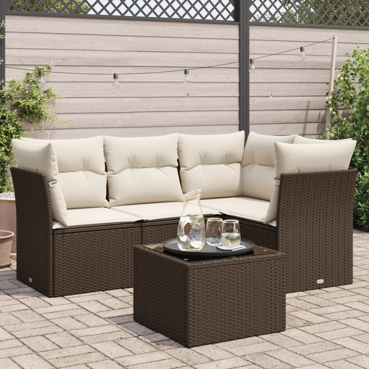 Set divano in vimini marrone con cuscini color crema, tavolino e bevande su un patio.