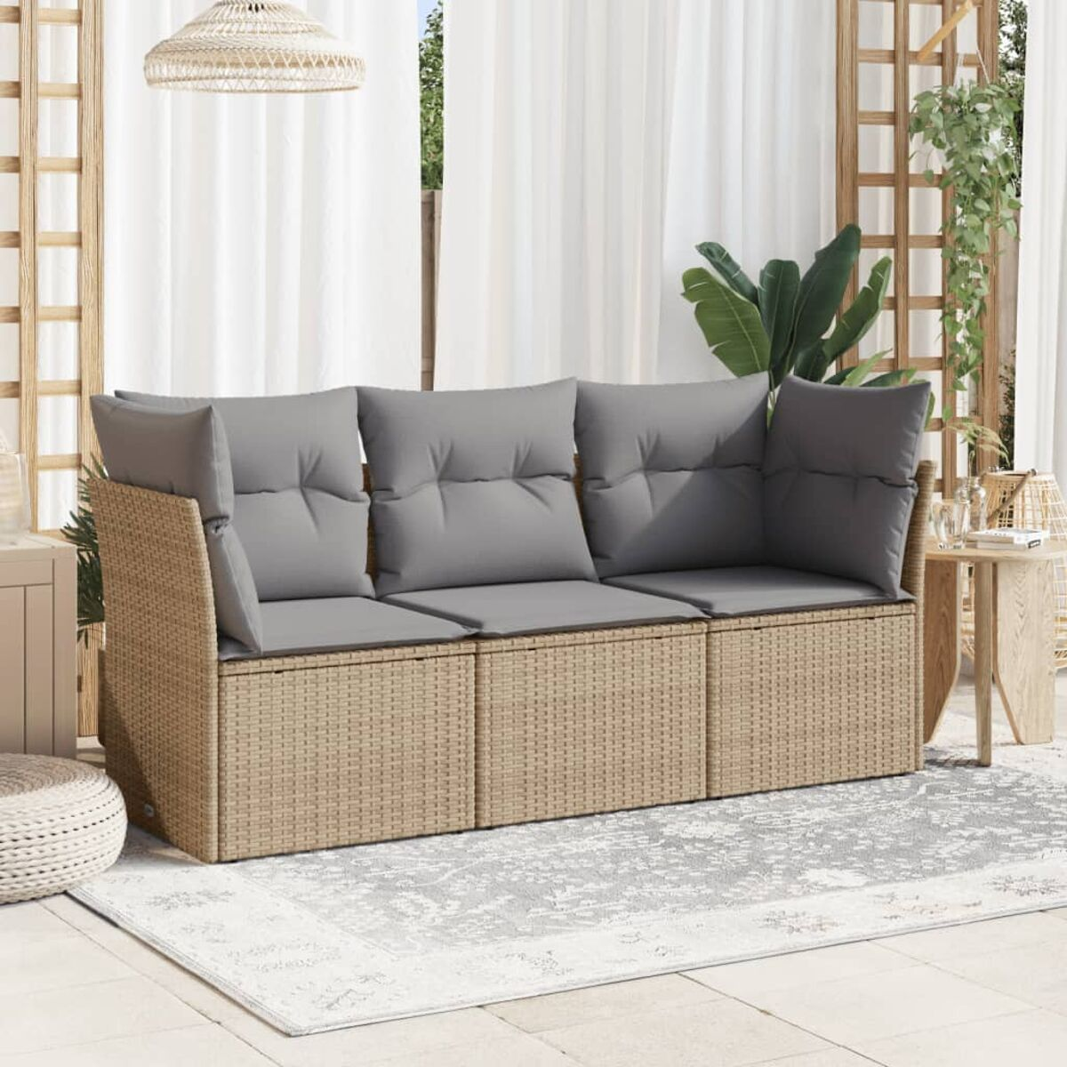 Beiges Rattan-Sofa mit grauen Kissen auf einer Terrasse mit Teppich und Vorhängen.