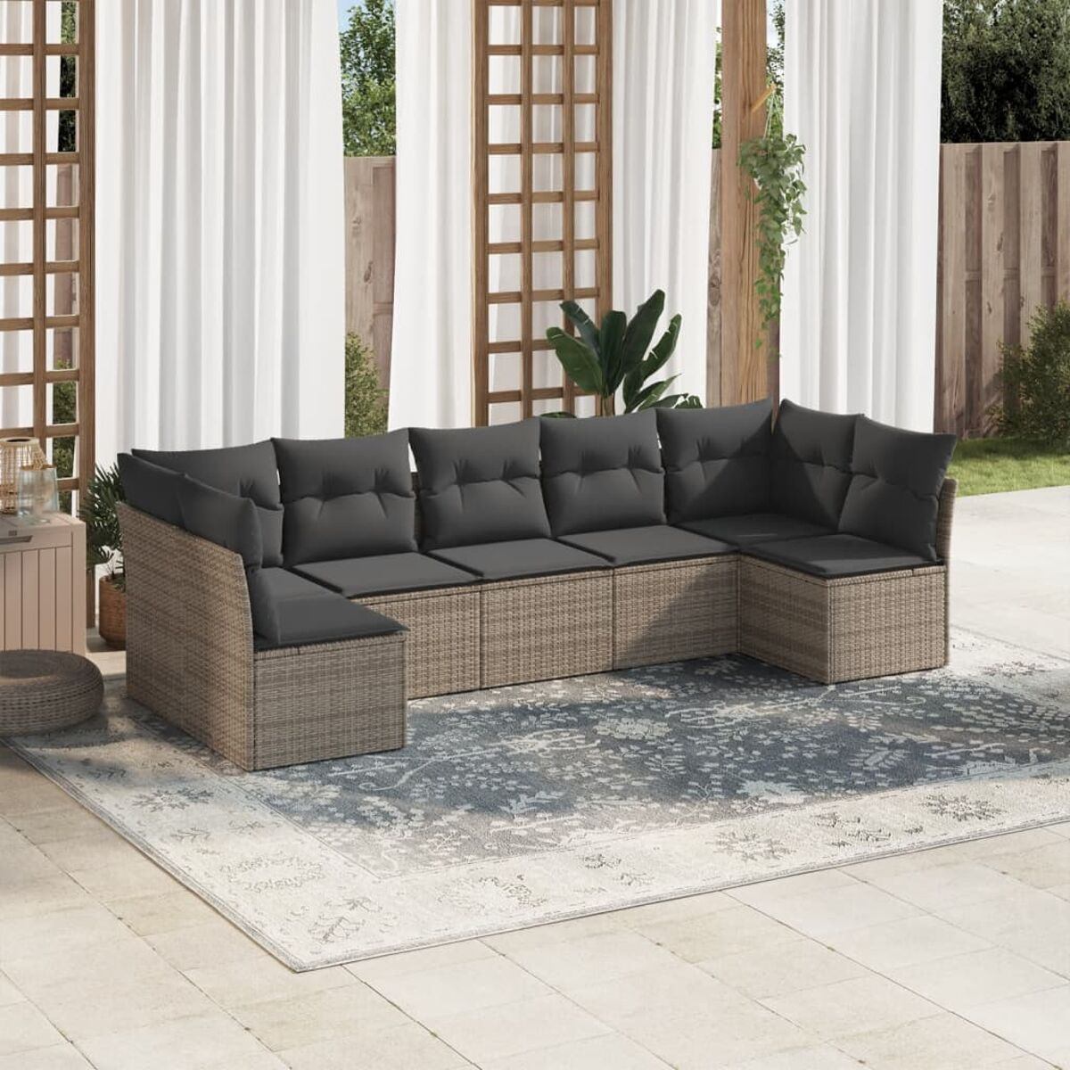 Rattan-Sofa-Set für den Außenbereich mit grauen Kissen auf einem gemusterten Teppich, weiße Vorhänge im Hintergrund.