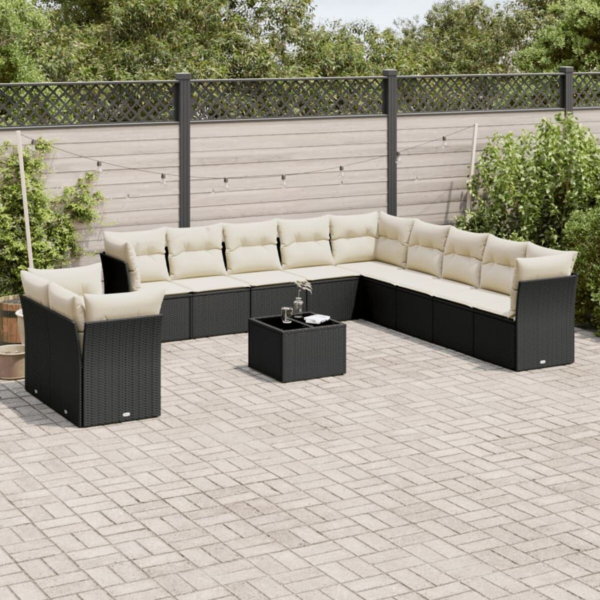 Schwarzes Rattan-Ecksofa mit beigen Kissen auf einer Terrasse. Ein kleiner Tisch steht mittendrin.