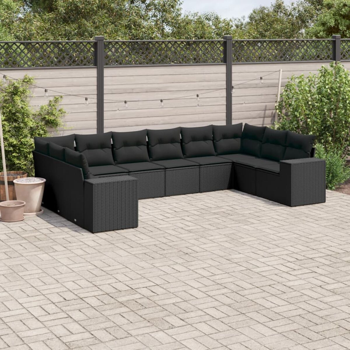 Schwarzes Rattan-Ecksofa mit schwarzen Kissen im Freien auf einer Ziegelterrasse.