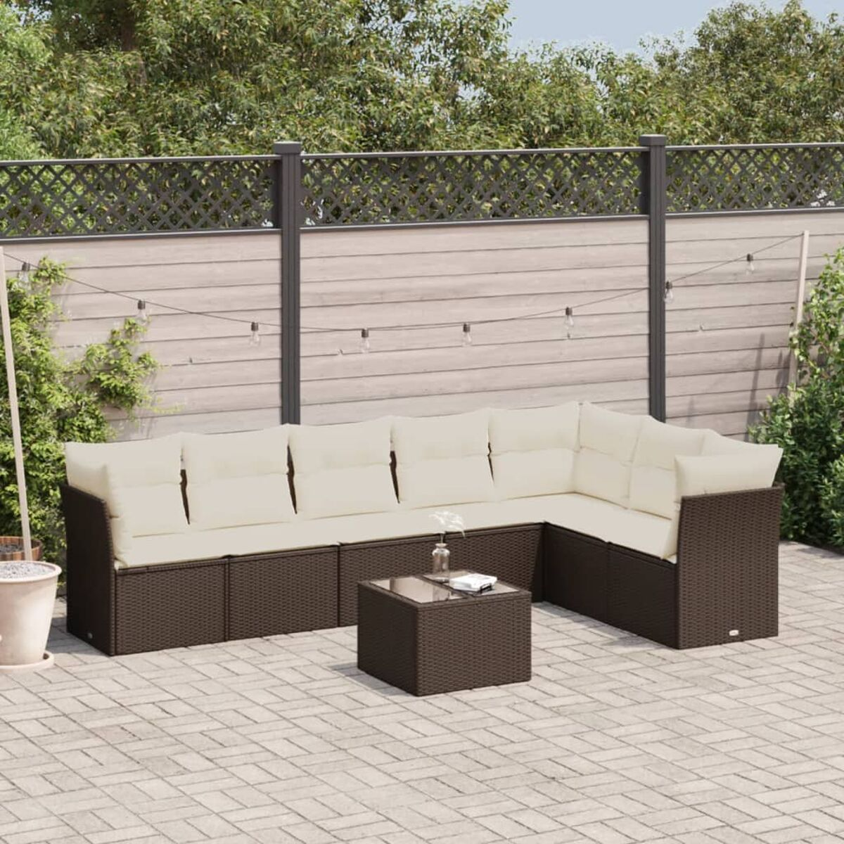 Un divano componibile da esterno in rattan marrone con cuscini color crema e tavolino in vetro.