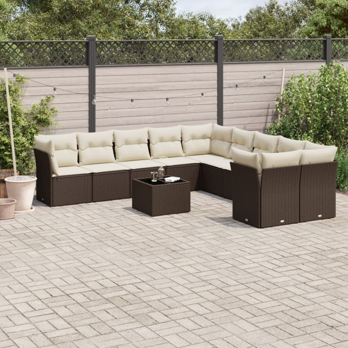 Divano componibile in vimini marrone con cuscini color crema e tavolo quadrato su un patio in mattoni.