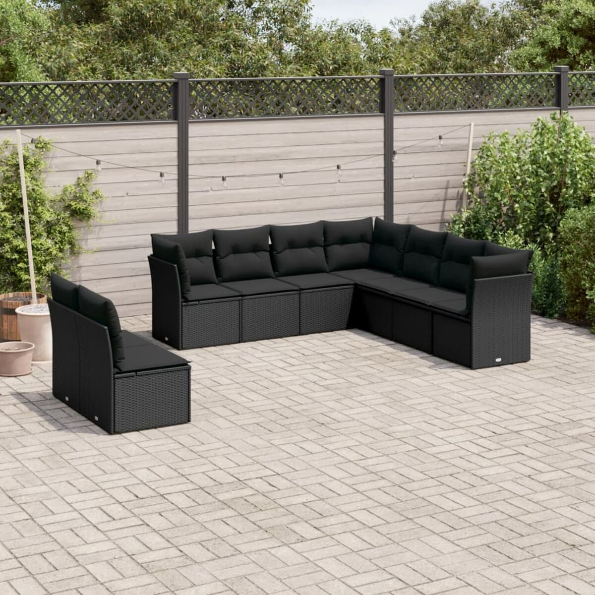 Schwarzes Rattan-Outdoor-Sofa-Set auf einer Terrasse. Enthält einen Hintergrund aus Grün und Zäunen.