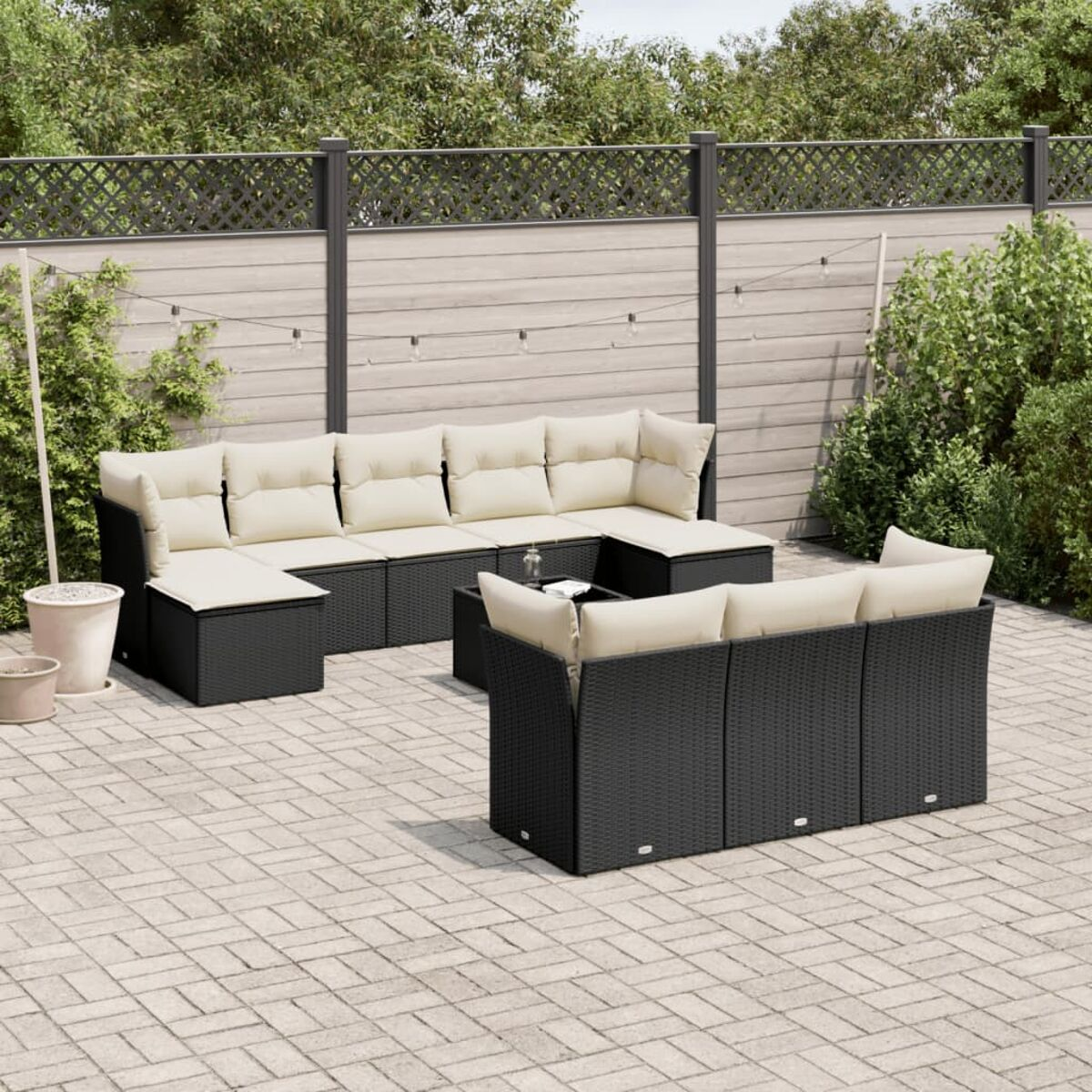 Gartenmöbel-Set, schwarzes Rattan, mit Kissen. Im Hintergrund ein Zaun und Pflanzen.