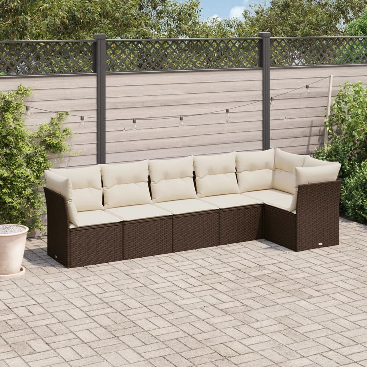 Divano componibile da esterno con cuscini color crema. È su un patio con una recinzione e vegetazione sullo sfondo.