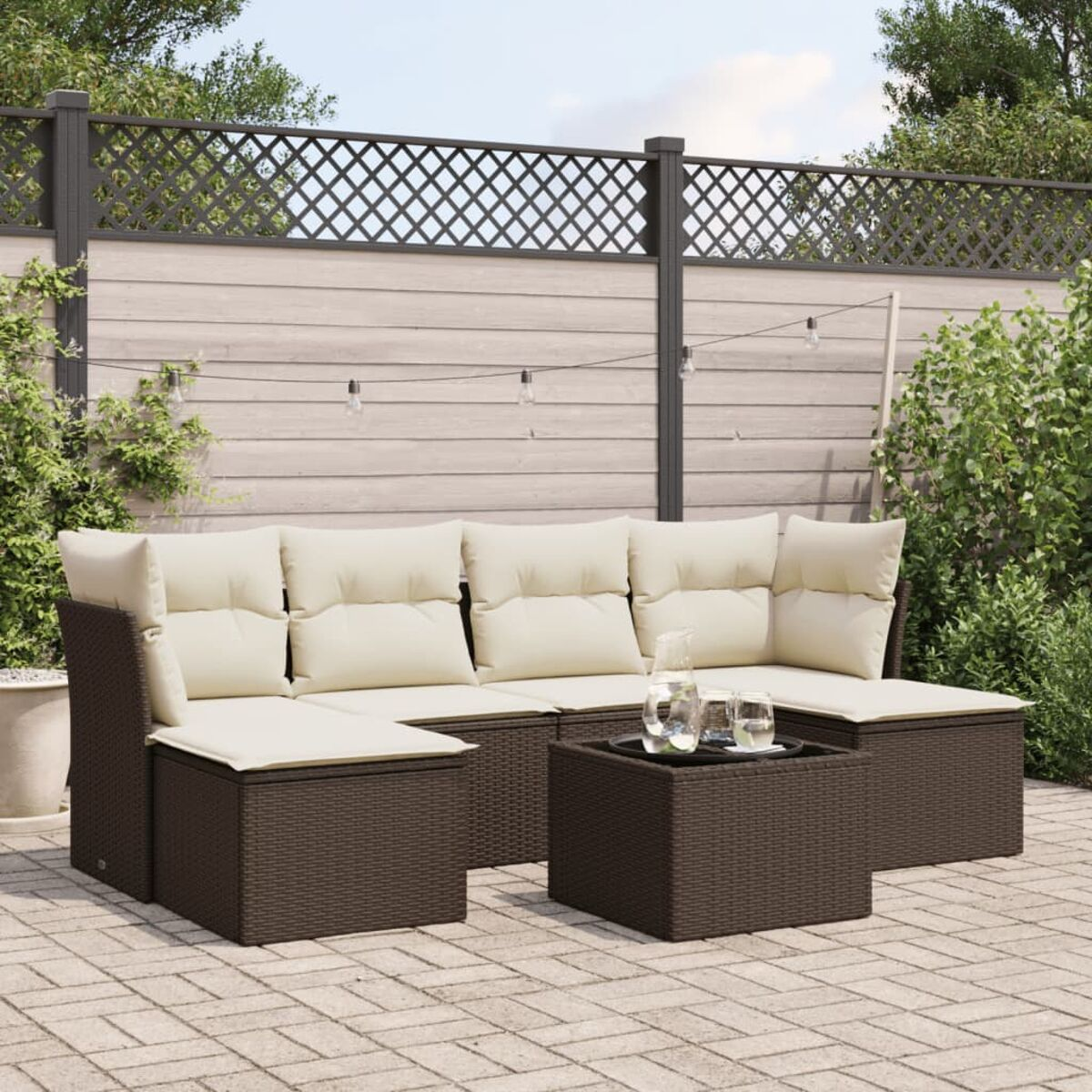 Set divano in vimini marrone scuro con cuscini color crema e un tavolo con piano in vetro. Lo sfondo è un patio.