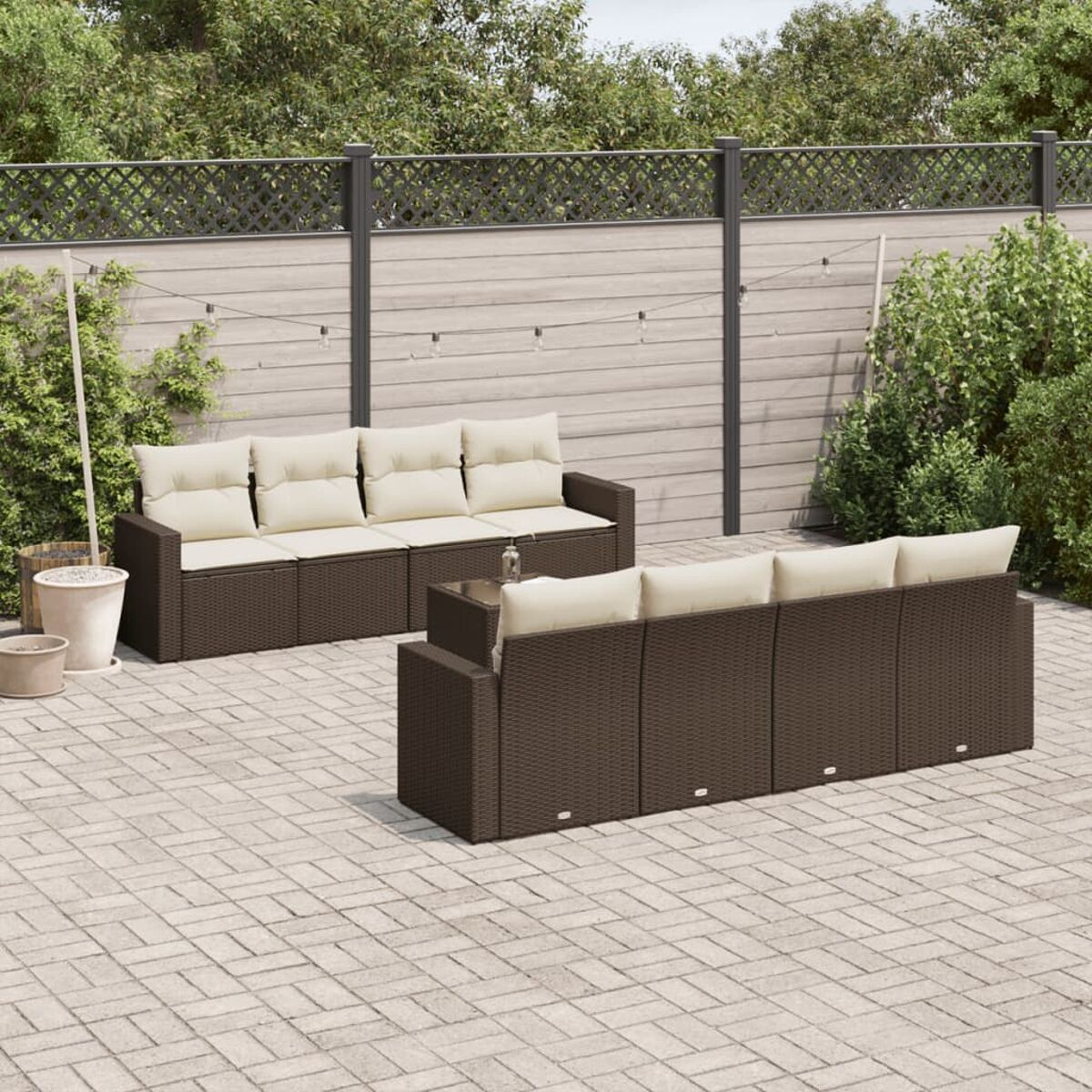 Braunes Rattansofa-Set mit cremefarbenen Kissen und einem kleinen Tisch auf einer Ziegelterrasse, mit Holzzaun.