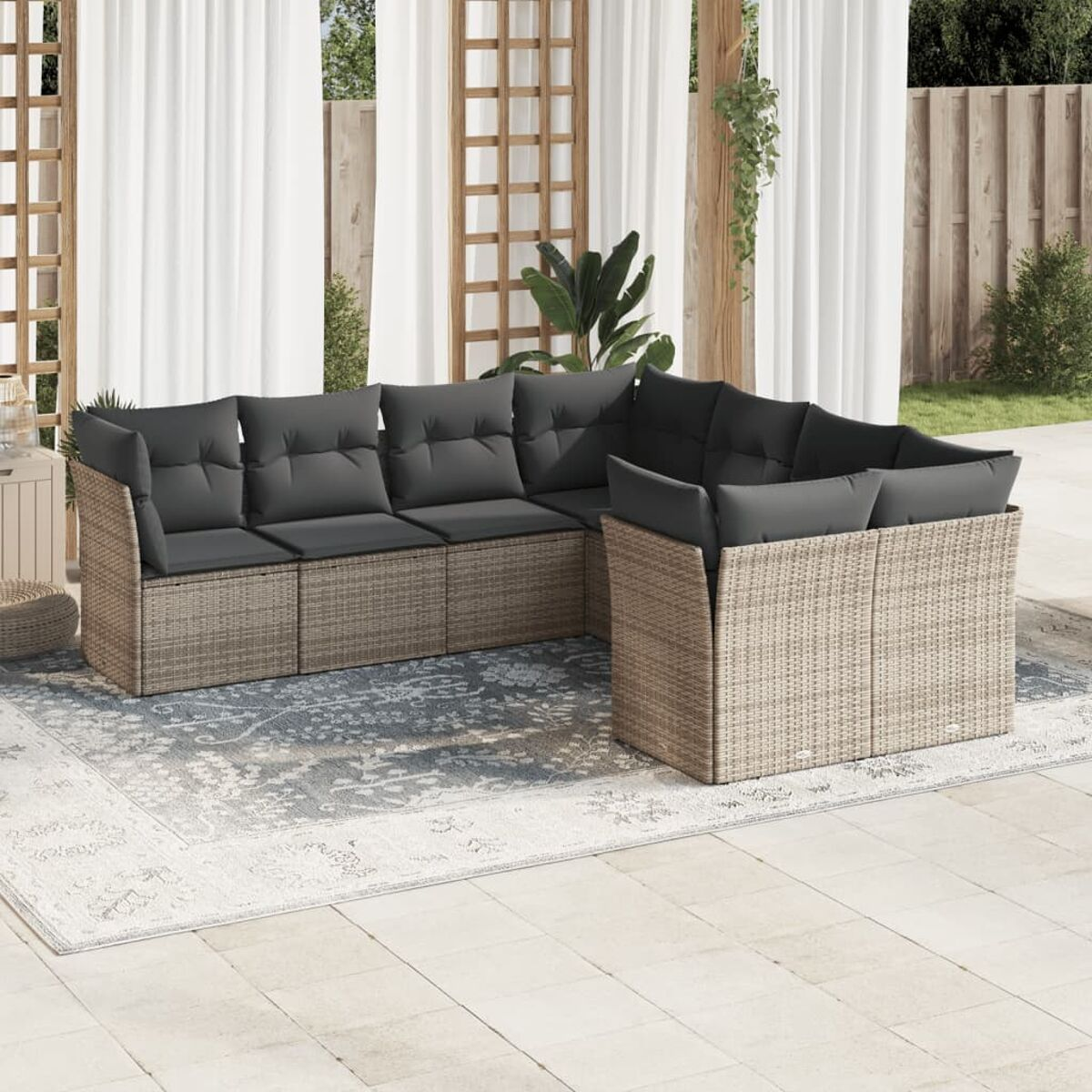 Rattan-Ecksofa mit dunkelgrauen Kissen auf einem gemusterten Teppich im Freien.