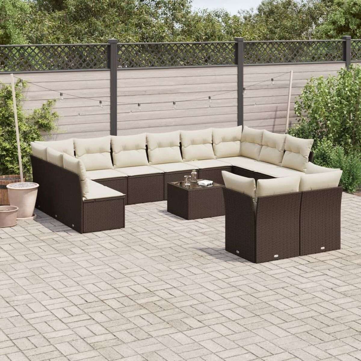 Divano angolare in rattan marrone con cuscini beige e tavolino. Il set da patio è su un patio in mattoni.