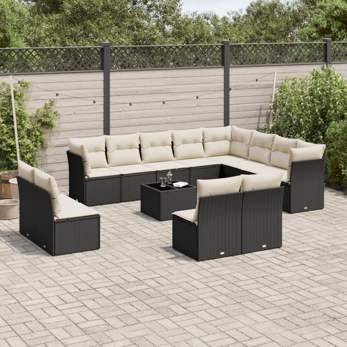 Schwarzes Rattan-Ecksofa mit cremefarbenen Kissen und Couchtisch auf einer Ziegelterrasse.