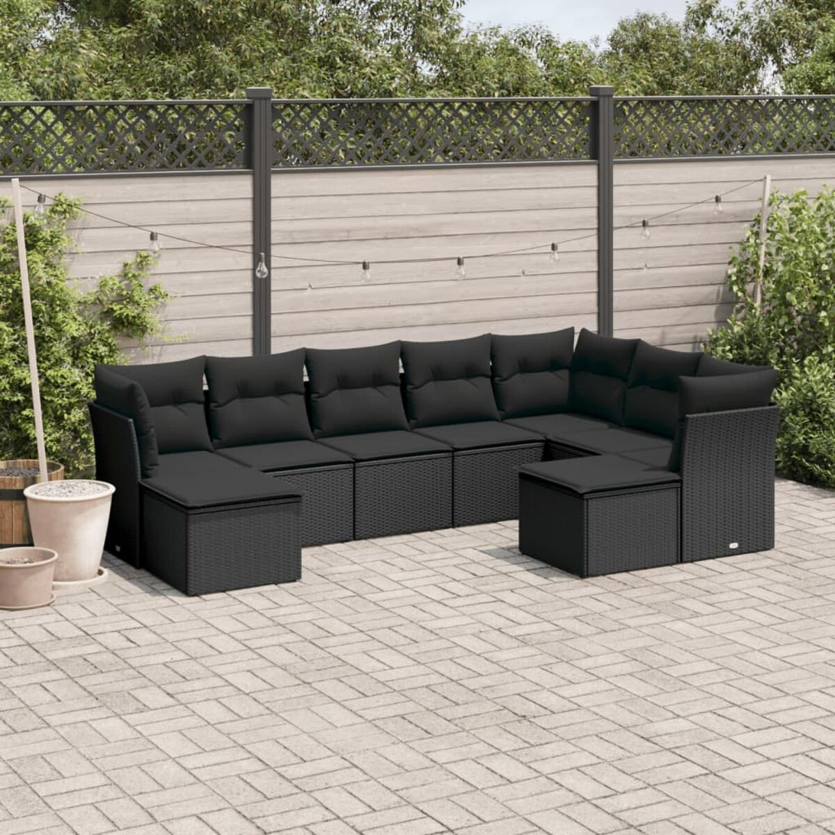 Schwarzes Outdoor-Ecksofa aus Korbgeflecht mit schwarzen Kissen. Inklusive Beistelltisch, auf Steinpflaster mit Zaun.