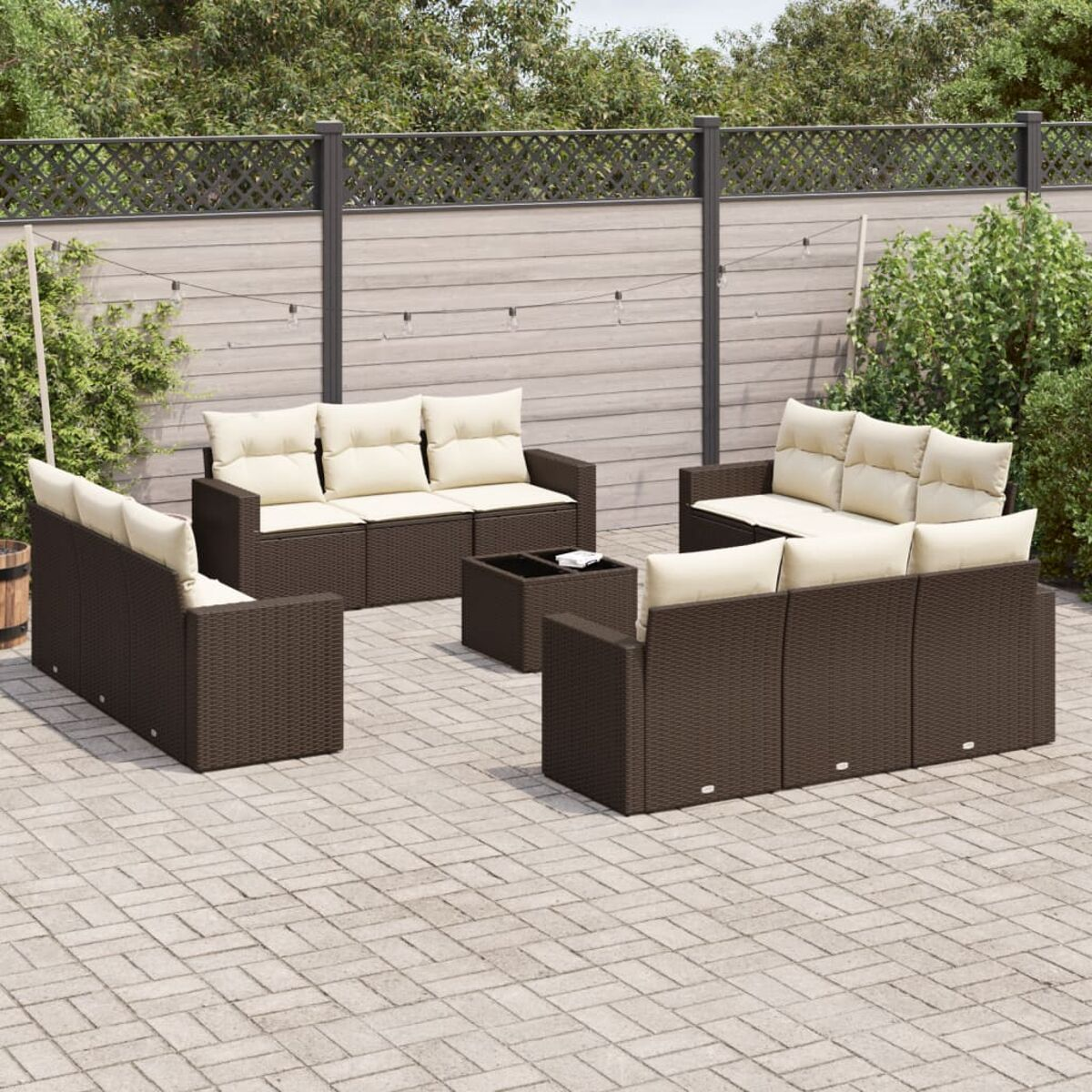 Set di divani da esterno in vimini marrone con cuscini color crema. Patio in mattoni, sfondo giardino.