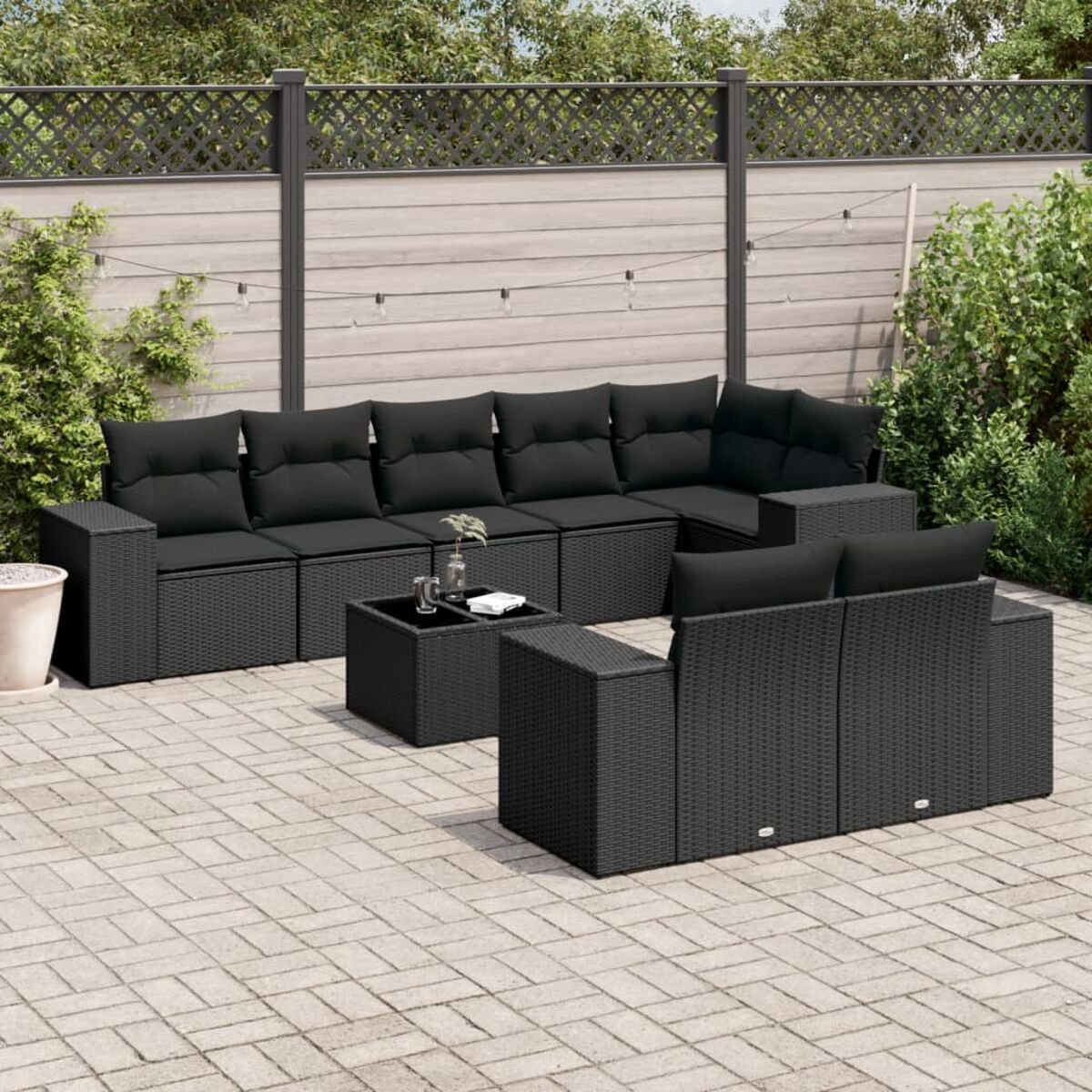 Outdoor-Ecksofa mit schwarzen Kissen und Tisch. Das Set steht auf einer gepflasterten Terrasse mit Zaun.