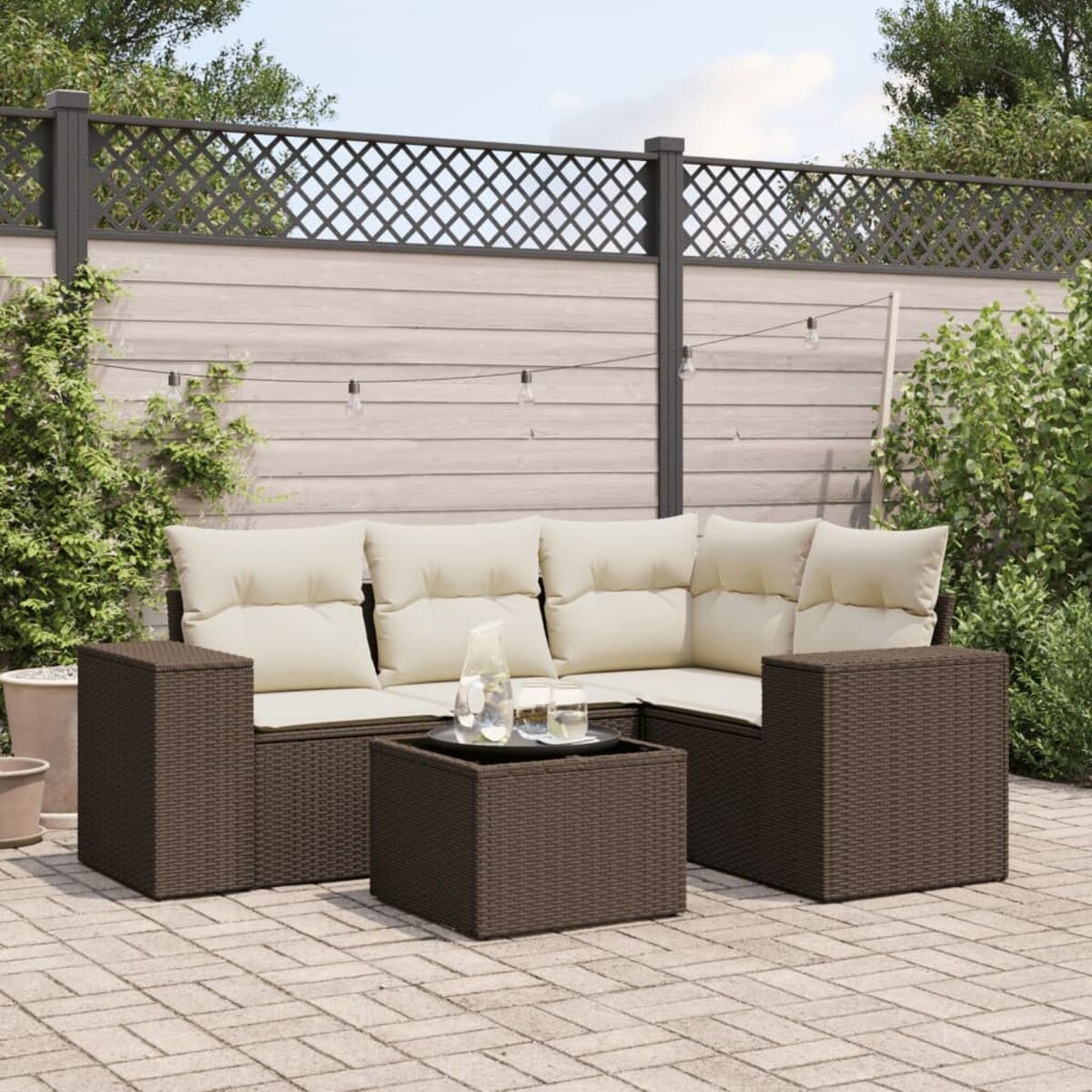 Braunes Rattan-Sofa-Set für den Außenbereich mit beigen Kissen, Tisch und zwei Stühlen auf einer Backstein-Terrasse, mit Zaun.