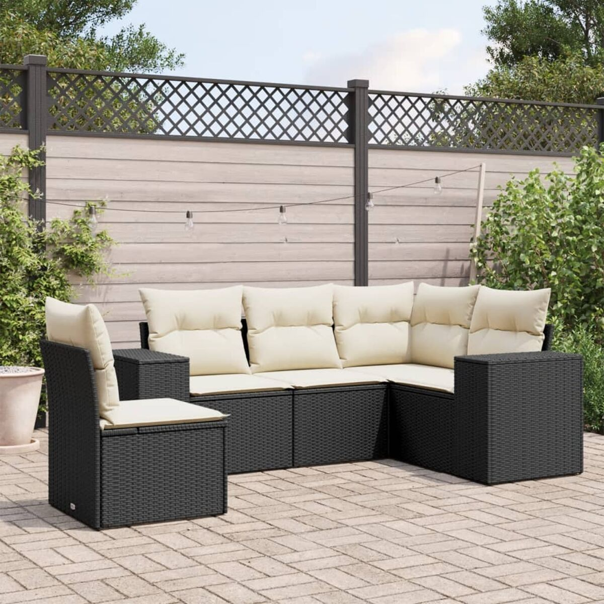 Schwarzes Ecksofa aus Rattan mit cremefarbenen Kissen und passendem Stuhl auf einer Ziegelterrasse.
