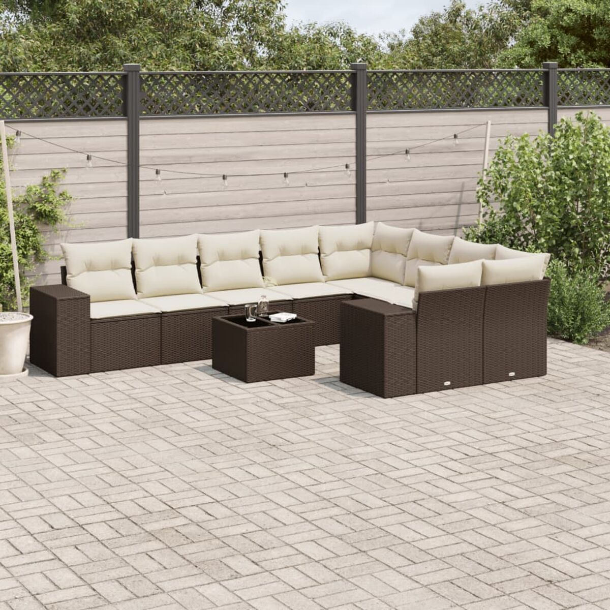 Set divano componibile in rattan con tavolo, cuscini color crema e piante. Ambiente esterno.