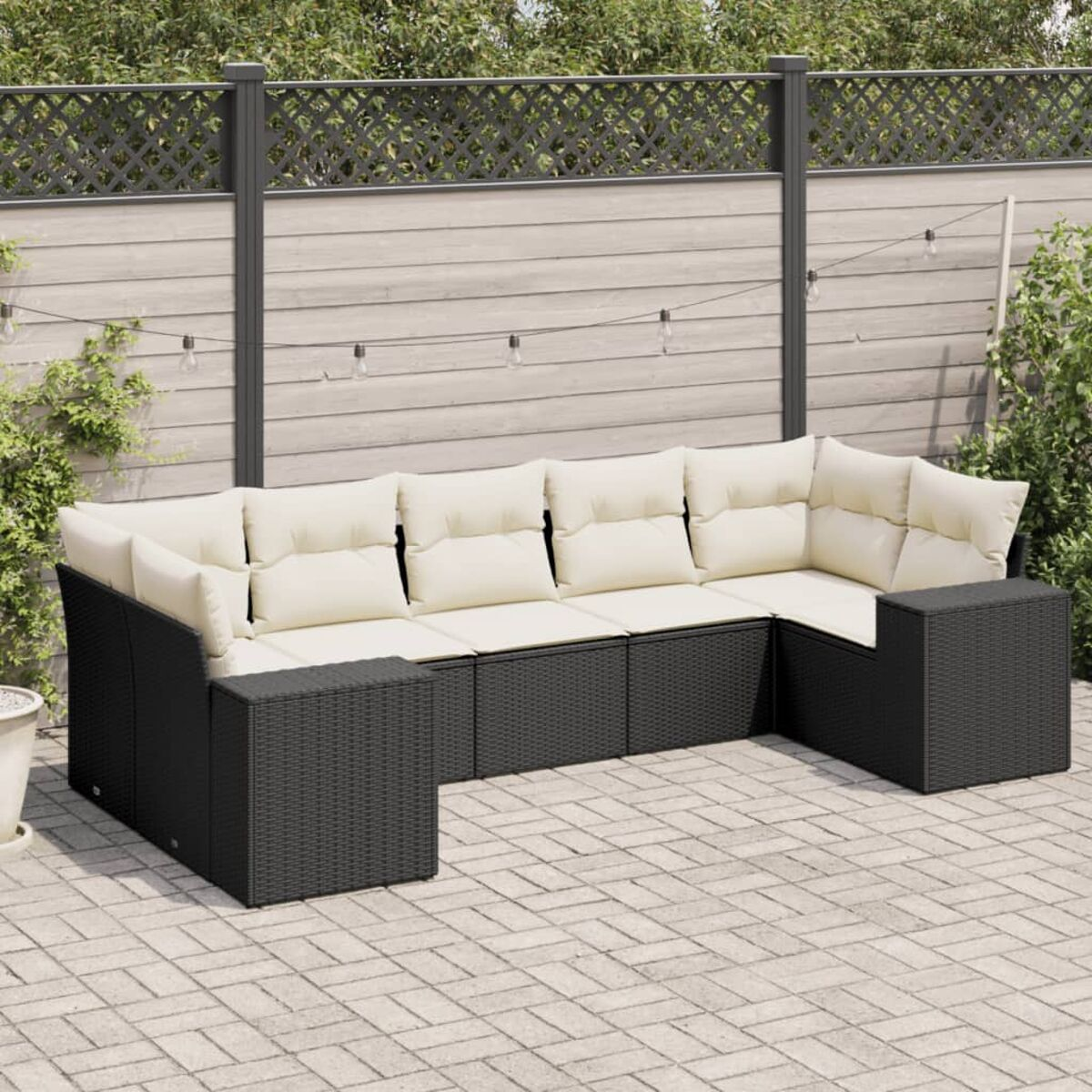 Schwarzes Ecksofa mit beigen Kissen. Ein Zaun, Pflanzen und eine Ziegelterrasse sind im Hintergrund.