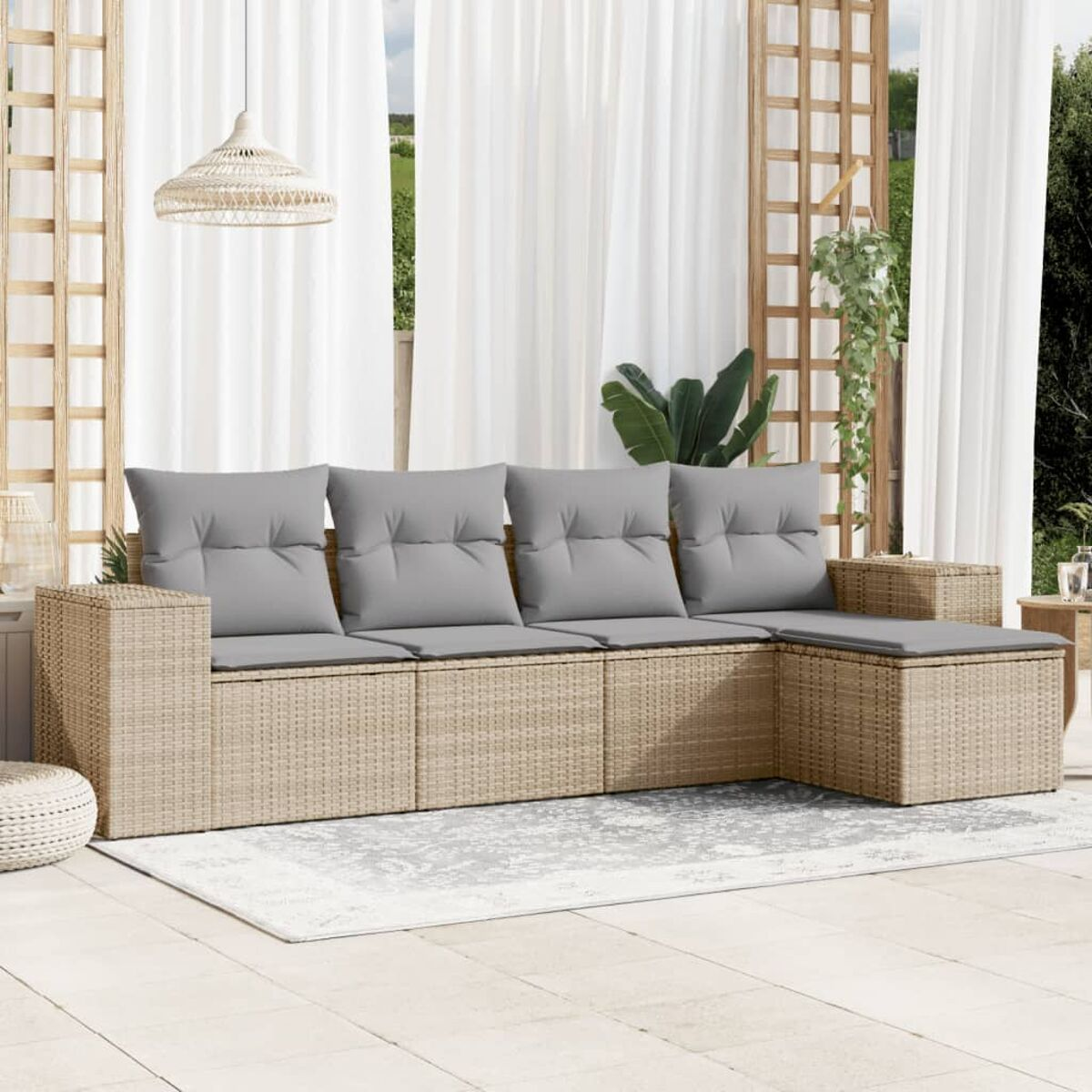 Beiges Rattan-Outdoor-Sofa mit grauen Kissen auf einem Terrassenteppich. Vorhänge und Pflanzen sind im Hintergrund.